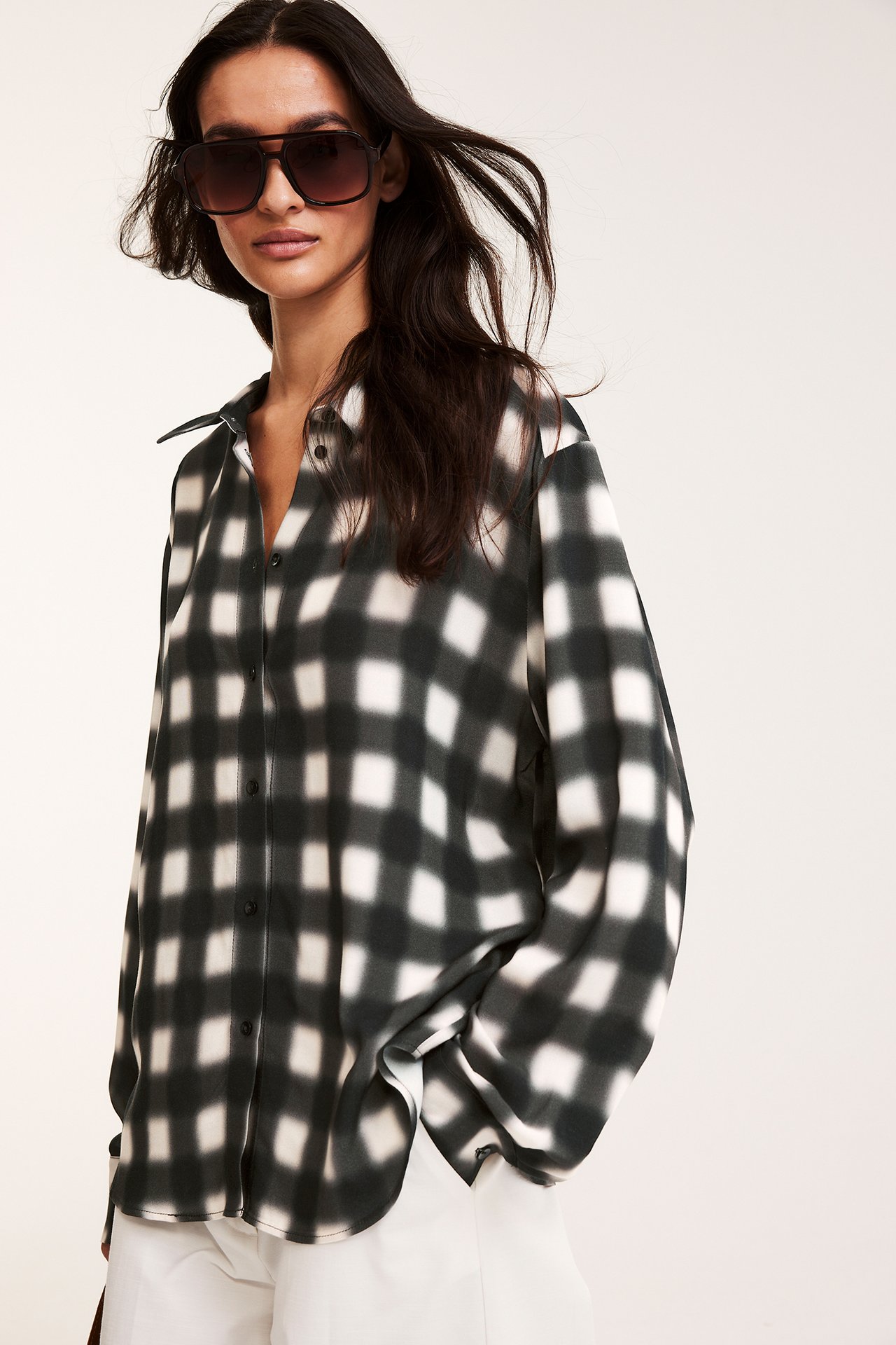Nainen edestä mustavalkoisessa ruudullisessa viskoosipaidassa, valkoisissa housuissa ja tummissa aurinkolaseissa.