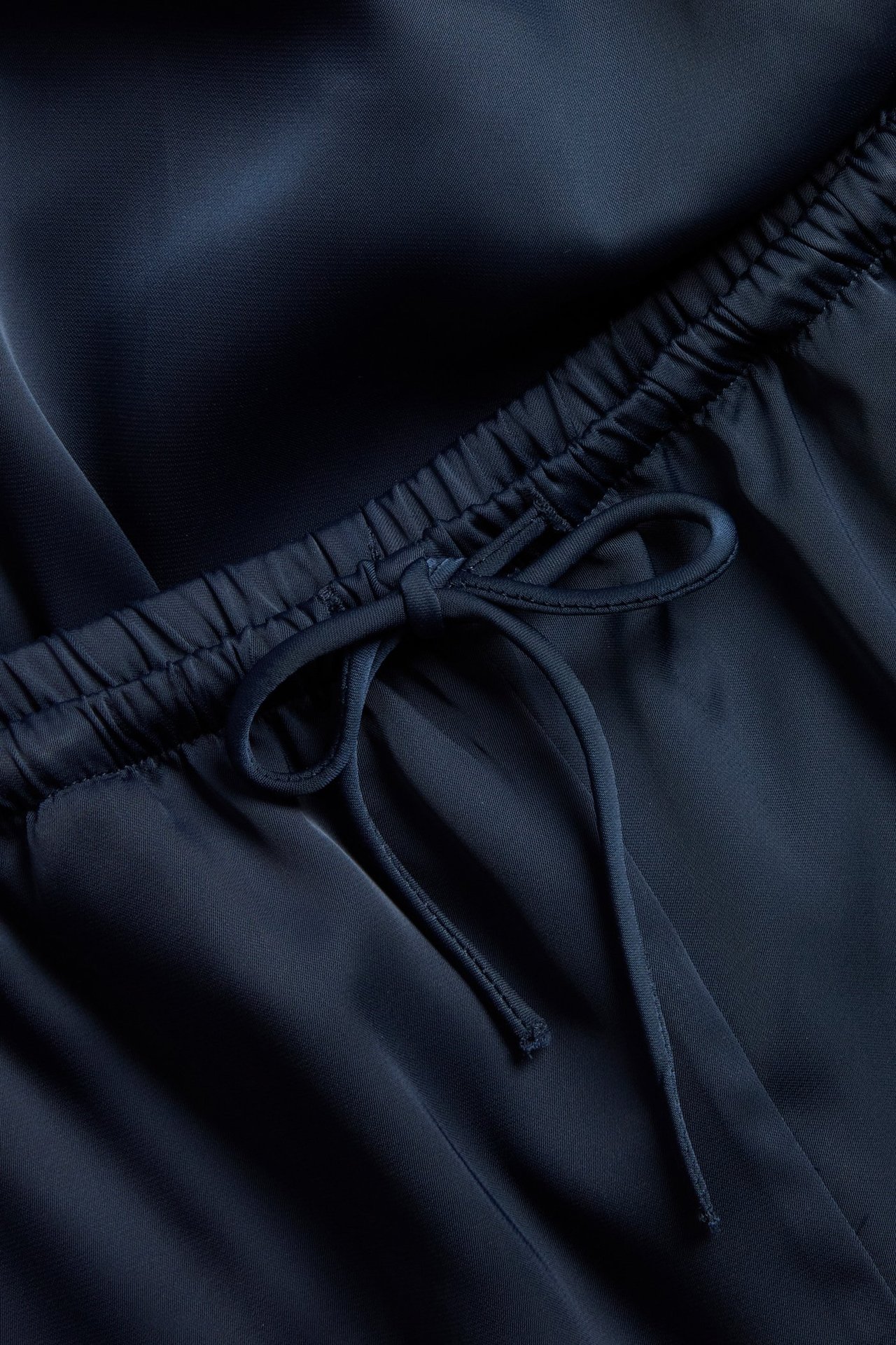 Närbild av mörkblå satinbyxor med resår i midjan och knuten dragsko.