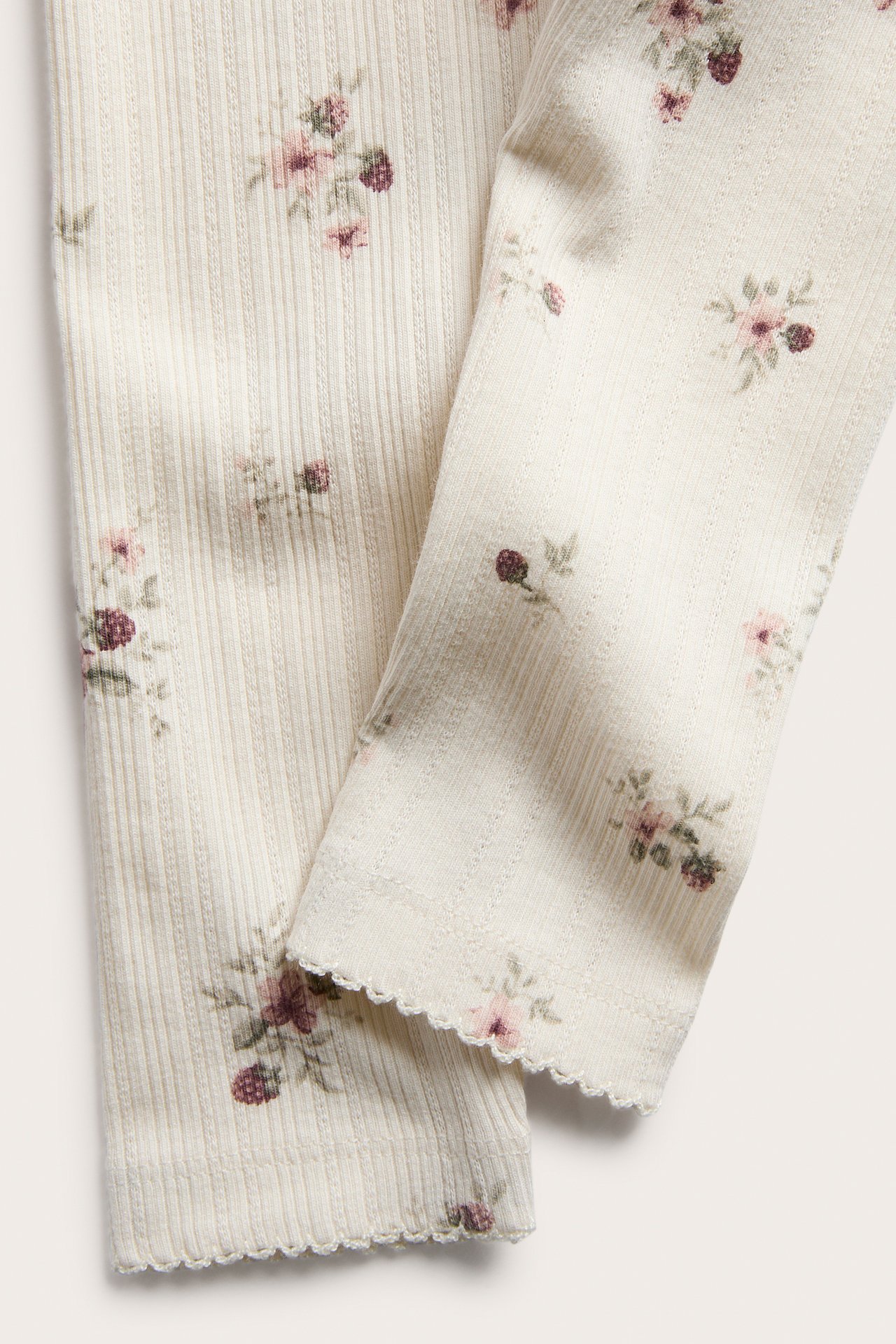 Närbild, benvit ribbad trikå med rosa blommönster och bär, vågiga kanter.