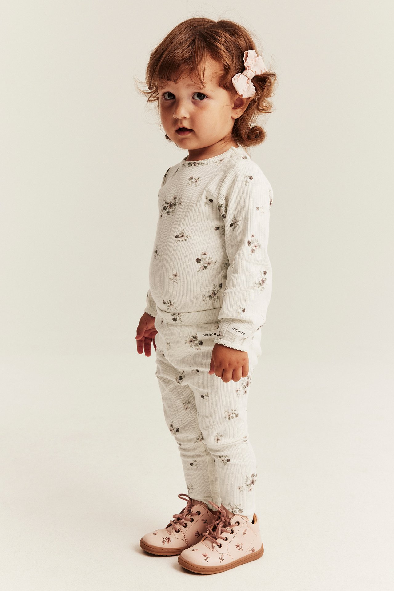 Sidovy av babyflicka i ribbad blommig långärmad topp, matchande leggings och rosa blommiga stövlar.