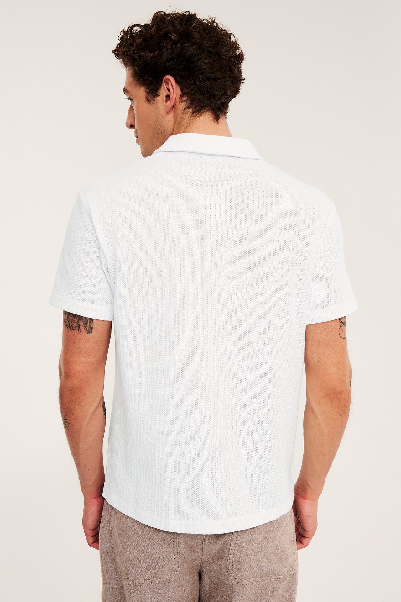 Ryggvy av man i en vit kortärmad pointelle-pikétröja och ljusbruna shorts.