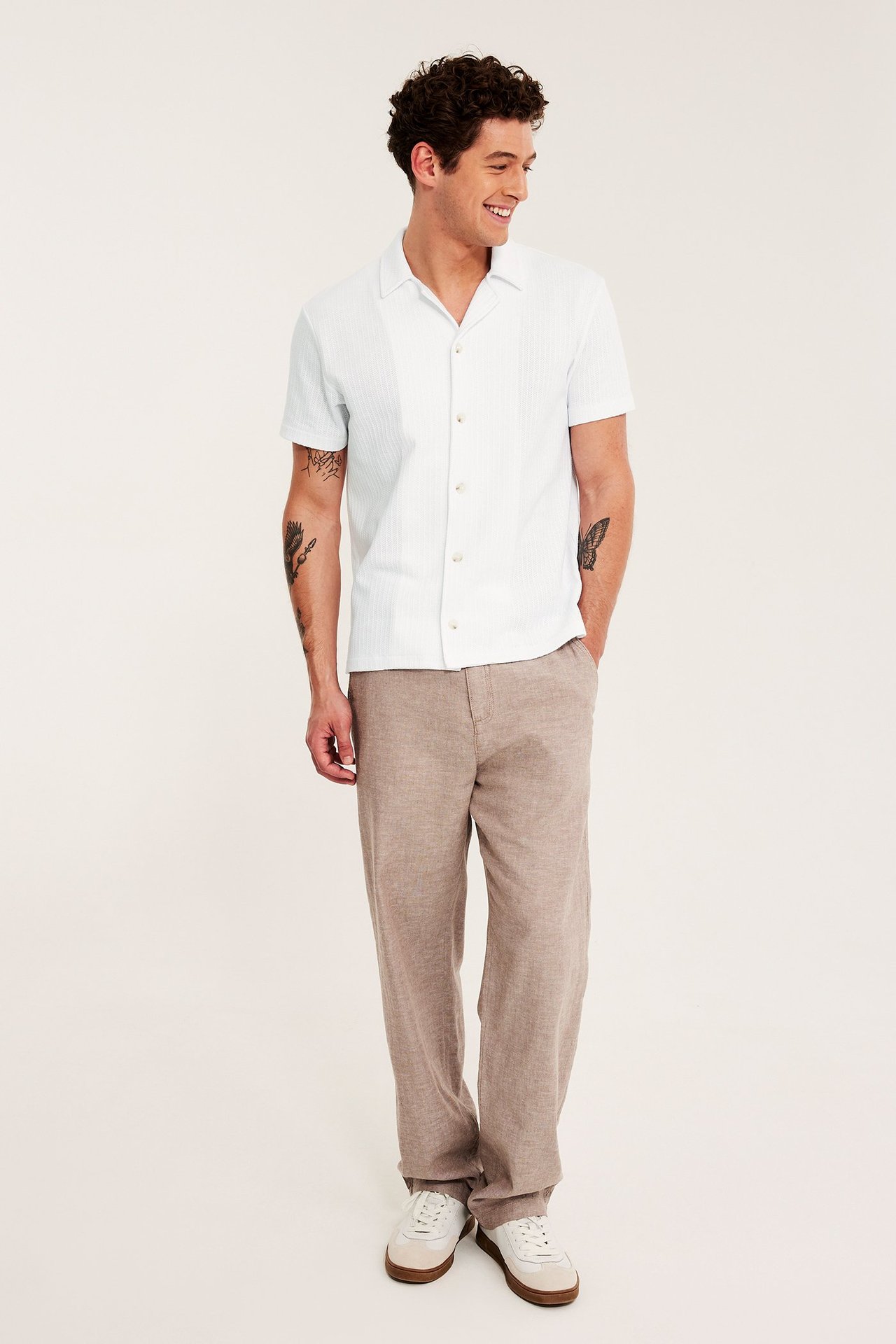 Forfra: mann i hvit kortermet pointelle-pikétrøye, beige bukser og hvite sneakers.