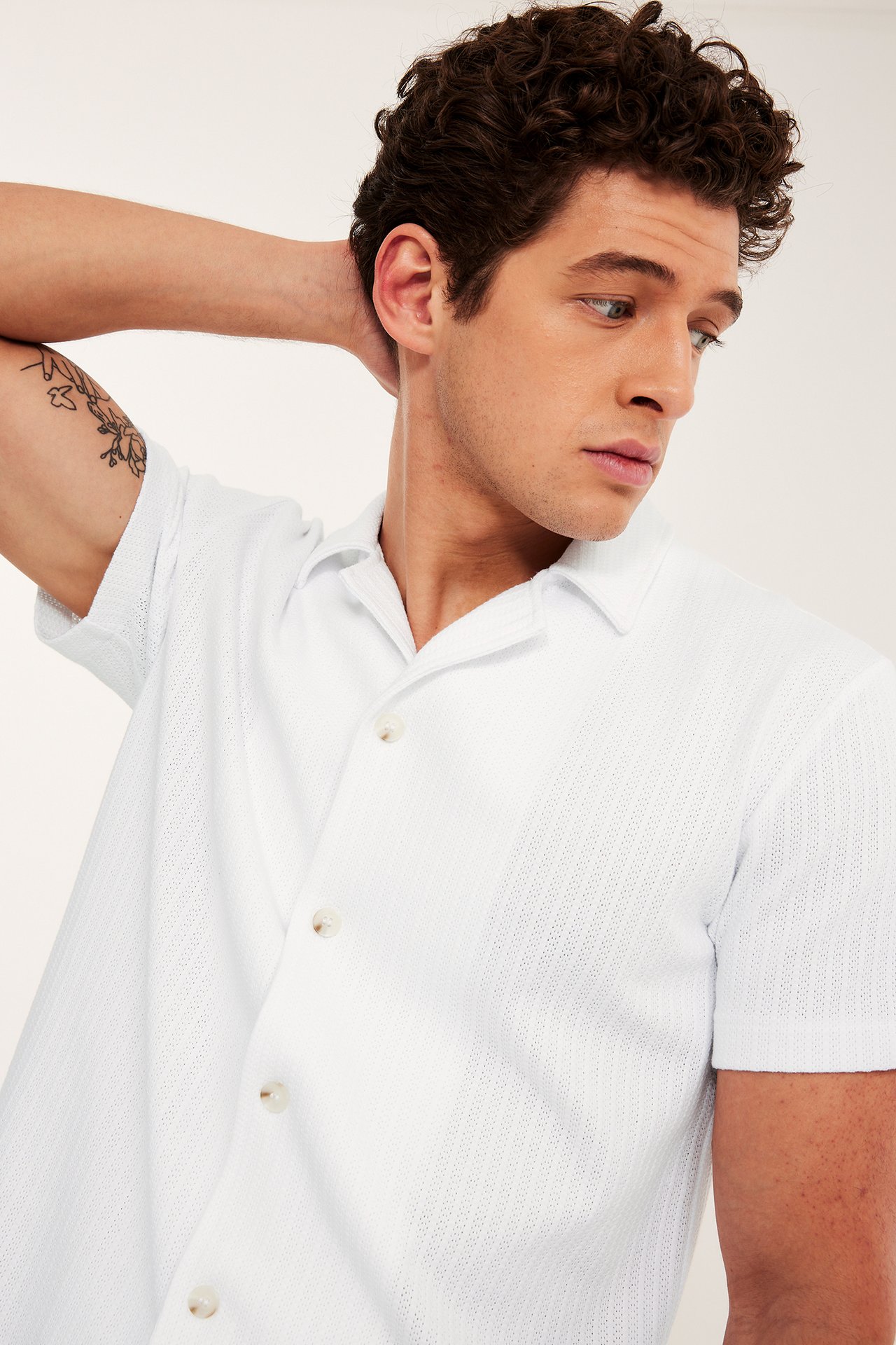 Frontvy av en man i en vit kortärmad pointelle-stickad pikétröja med resortkrage och knappar.