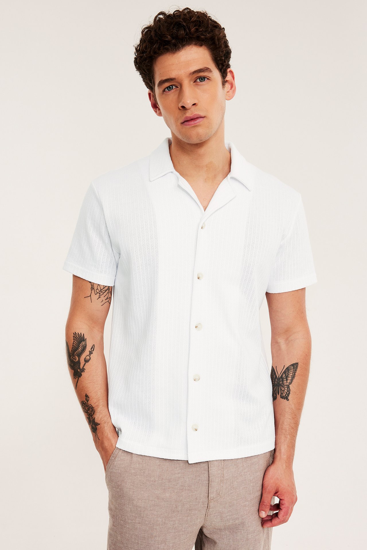 Frontvy av en man i vit pointelle pikétröja med resortkrage och beiga shorts.