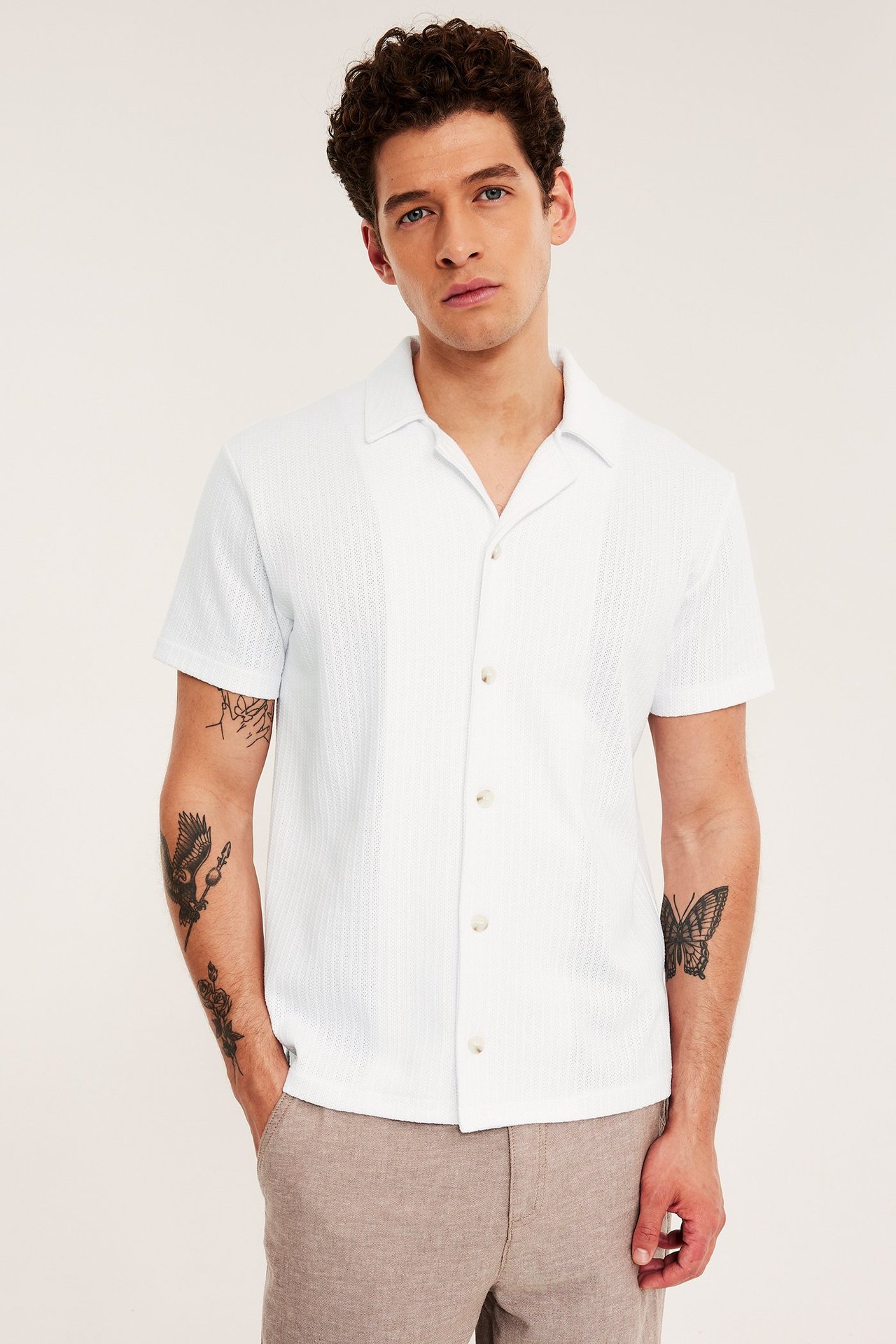 Frontbilde av en mann i hvit pointelle piké-skjorte med resort-krage og beige shorts.