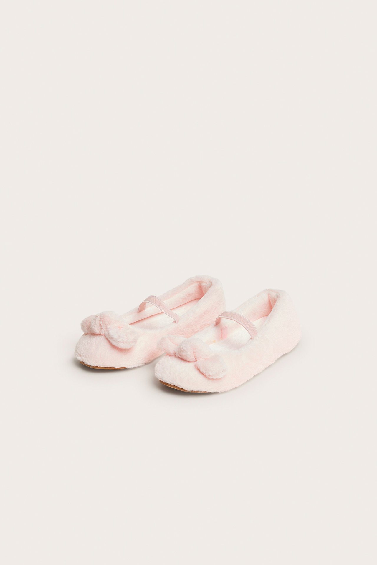Framåtvänd bild av rosa fluffiga ballerinatofflor med rosetter och resårband.