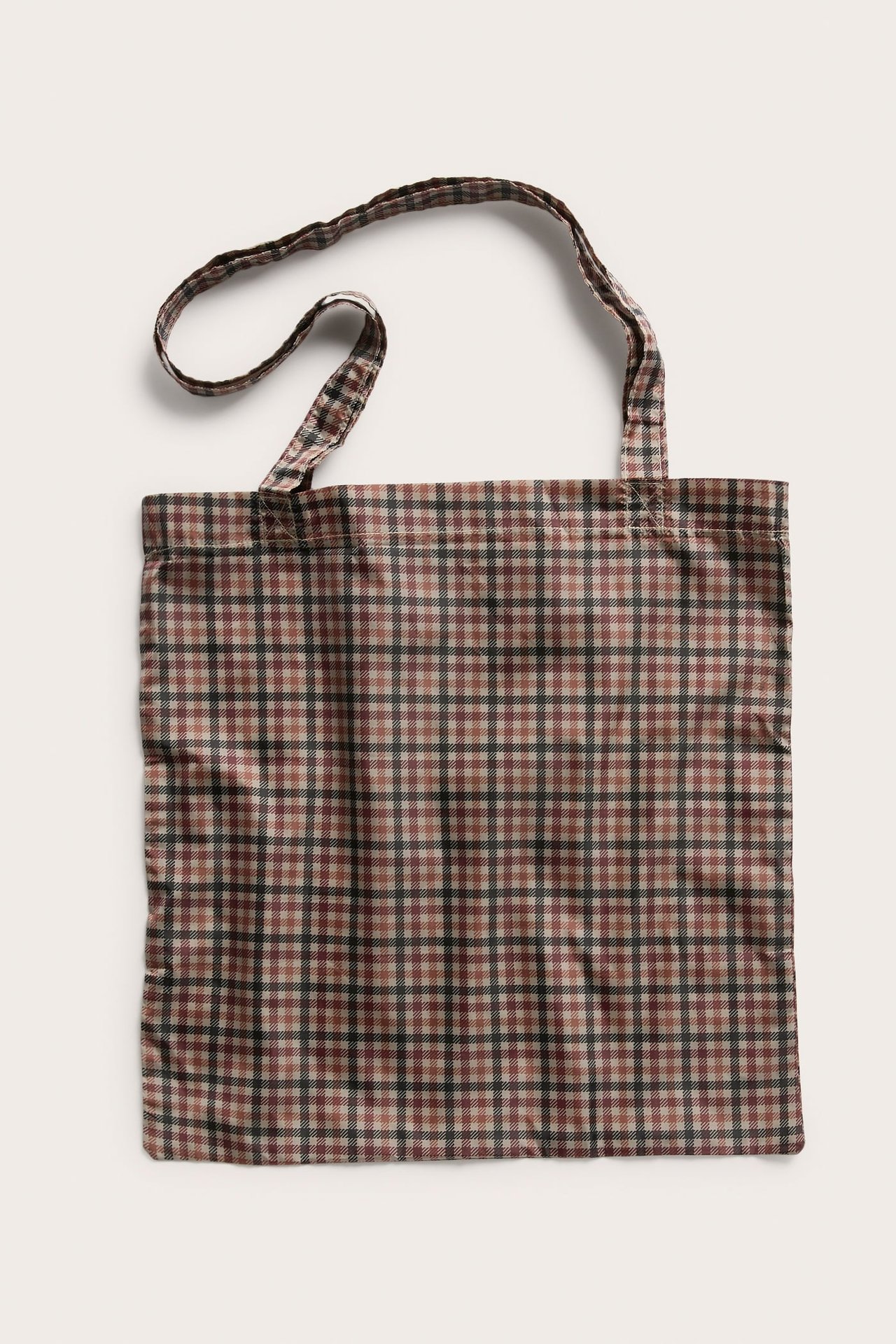 Frontbilde av en brun og beige rutete stoffveske med to håndtak.