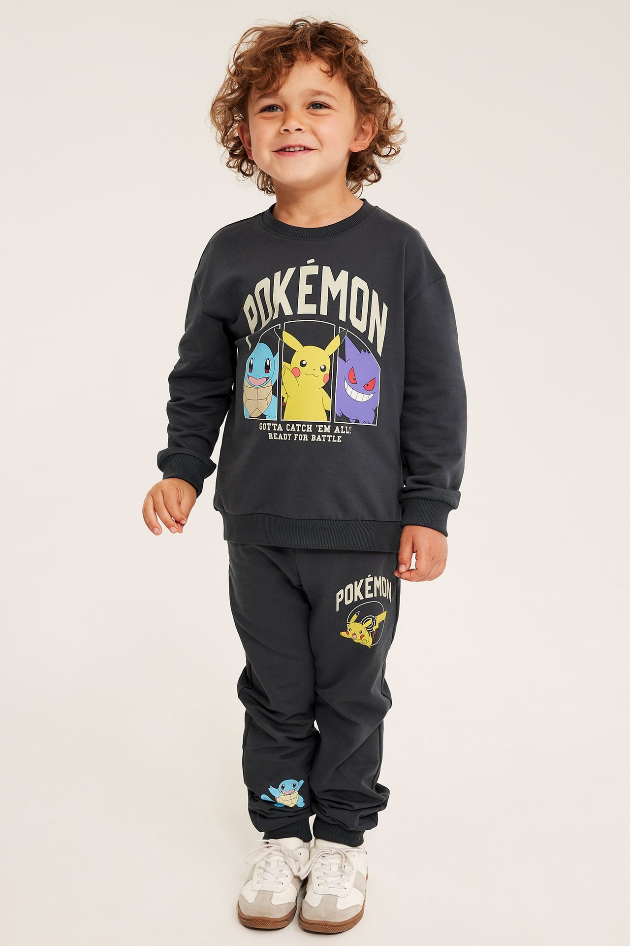Framifrån, ett barn i en mörkgrå Pokémon-tryckt sweatshirt och matchande mjukisbyxor.