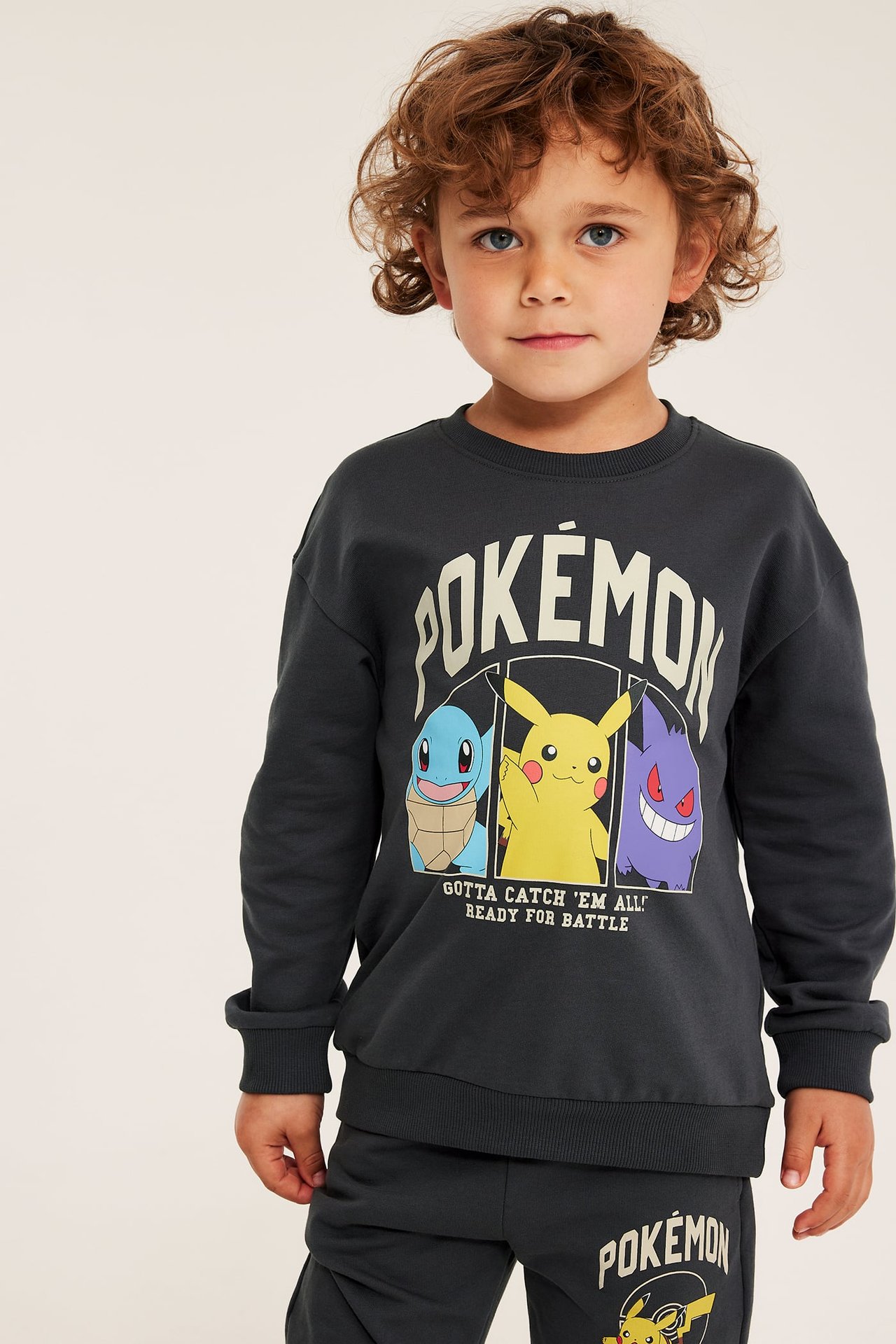 Frontvy: Barn i mörkgrå Pokémon-tröja med Squirtle, Pikachu, Gengar-tryck och matchande mjukisbyxor.