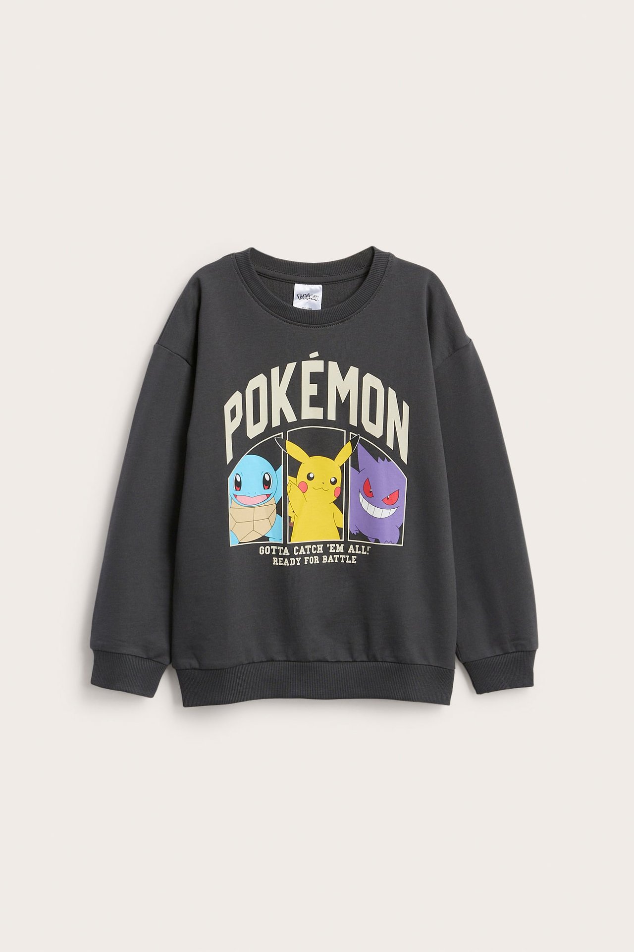 Framifrån, en mörkgrå barntröja med Pókemon-tryck föreställande Squirtle, Pikachu och Gengar.