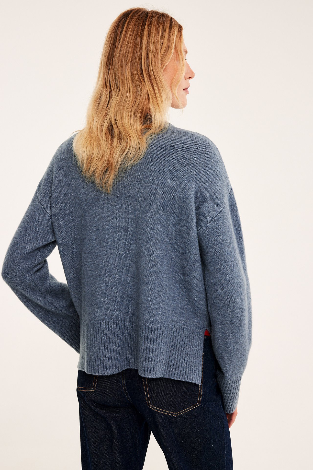 Bakfra kvinne i blå strikket løstsittende genser og mørkeblå jeans.