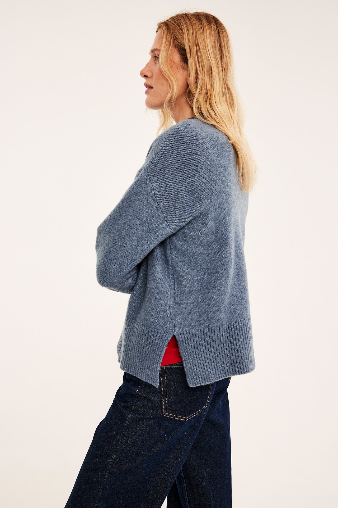 Sidebilde av kvinne i løs blå genser med splitter og mørkeblå jeans.