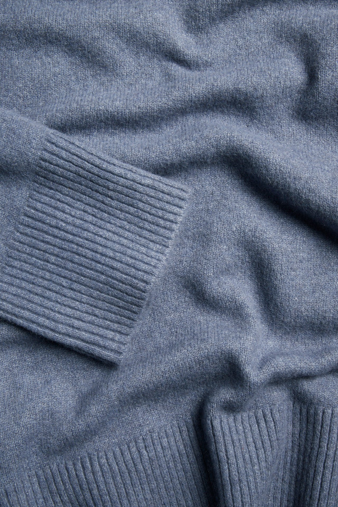 Närbild av en blåmelerad stickad pullover med ribbade muddar och nederkant.
