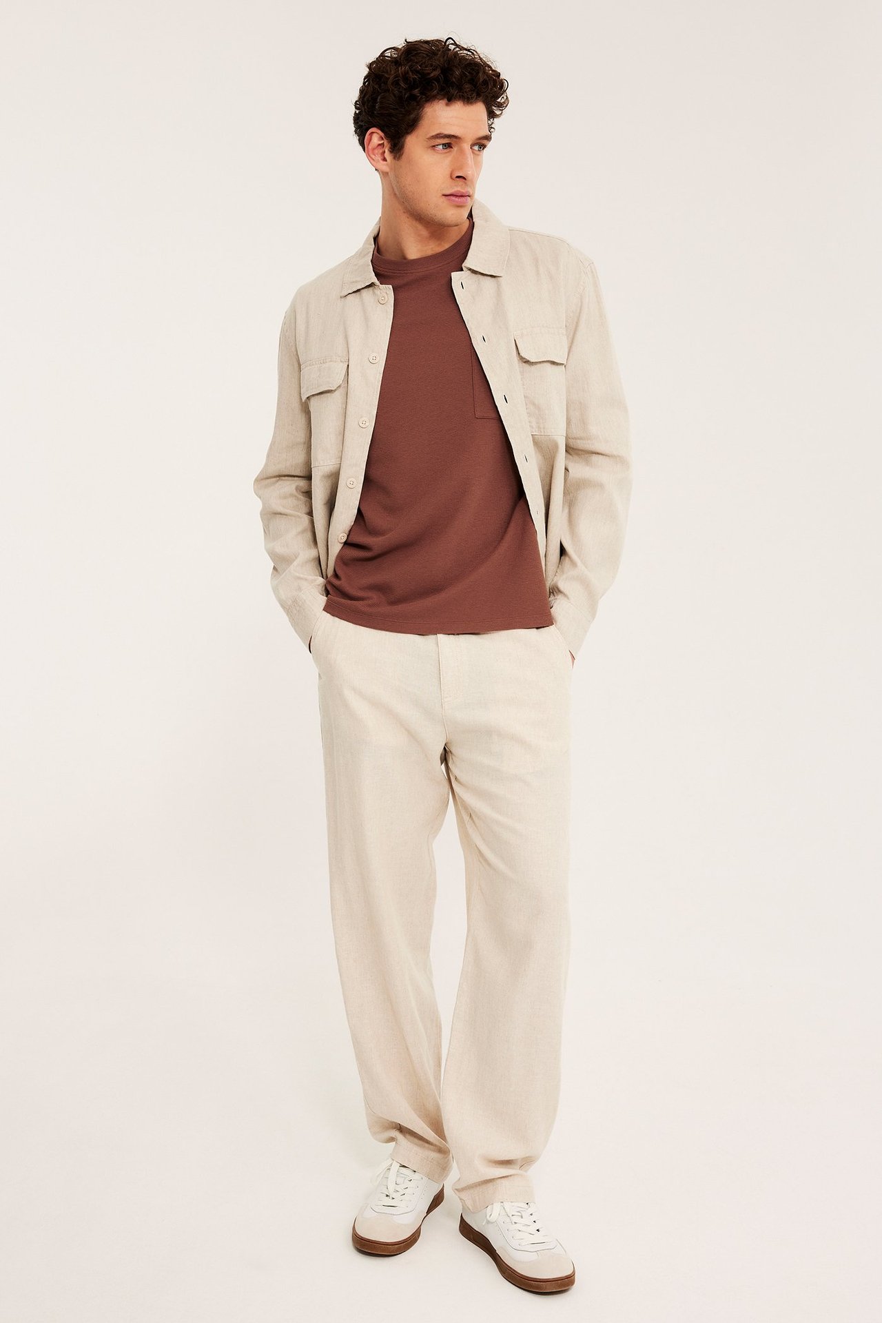 Frontvisning: mann i brun strukturert t-skjorte med lomme, brukt med beige overskjorte og bukser.