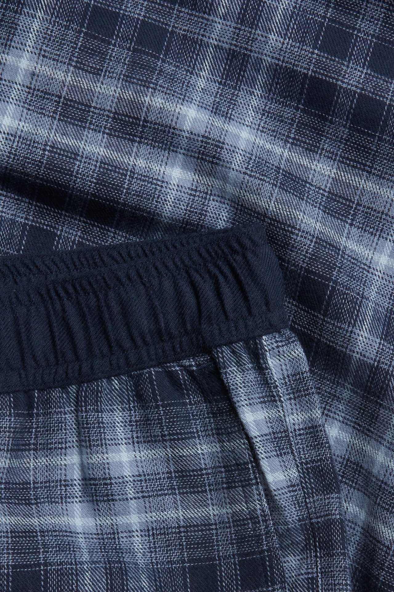 Nærbilde av blårutete pyjamasbukser med mørkeblå elastisk linning.