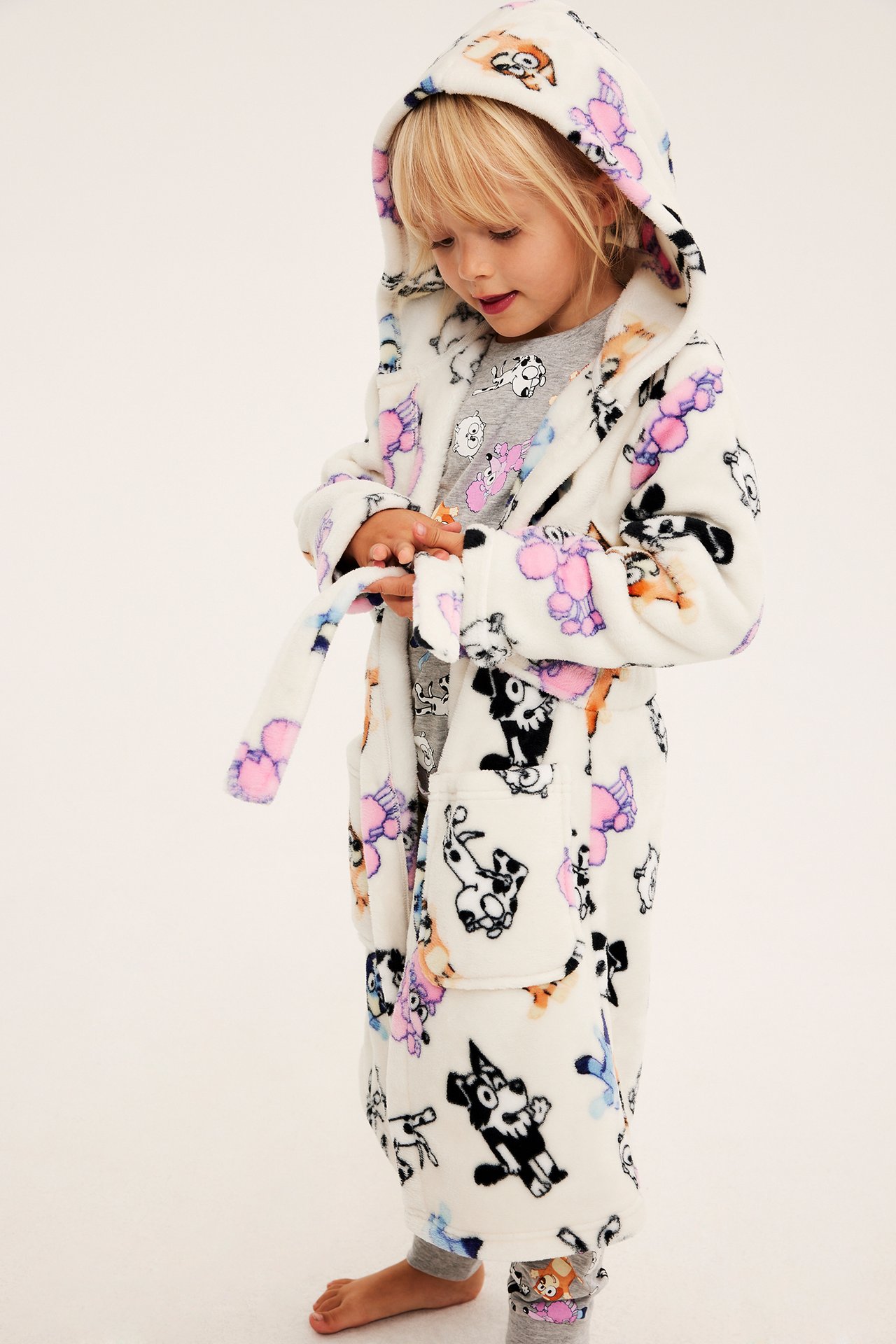 Sivukuva lapsesta valkoisessa hupullisessa kylpytakissa koiraprintillä ja harmaissa pyjamissa.