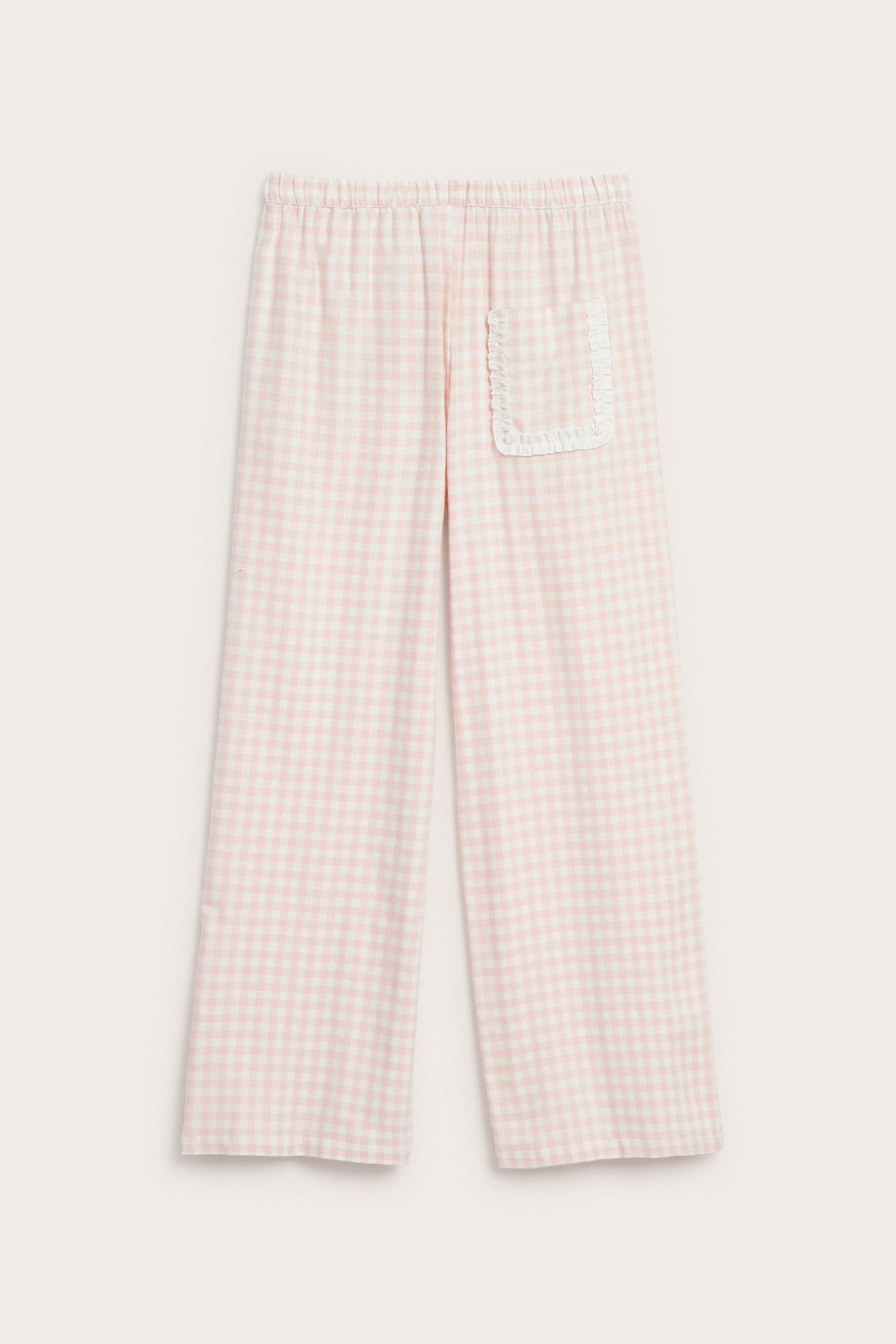 Edestä näkymä vaaleanpunaisista ja valkoisista ruudullisista pyjamahousuista, joissa on röyhelötasku.