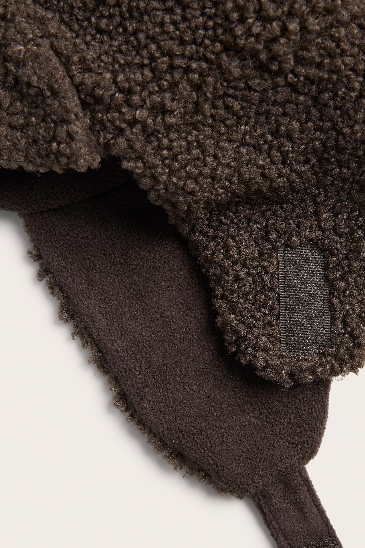 Närbild av en brun trapperhatt i fleece med texturerad utsida och slät insida.