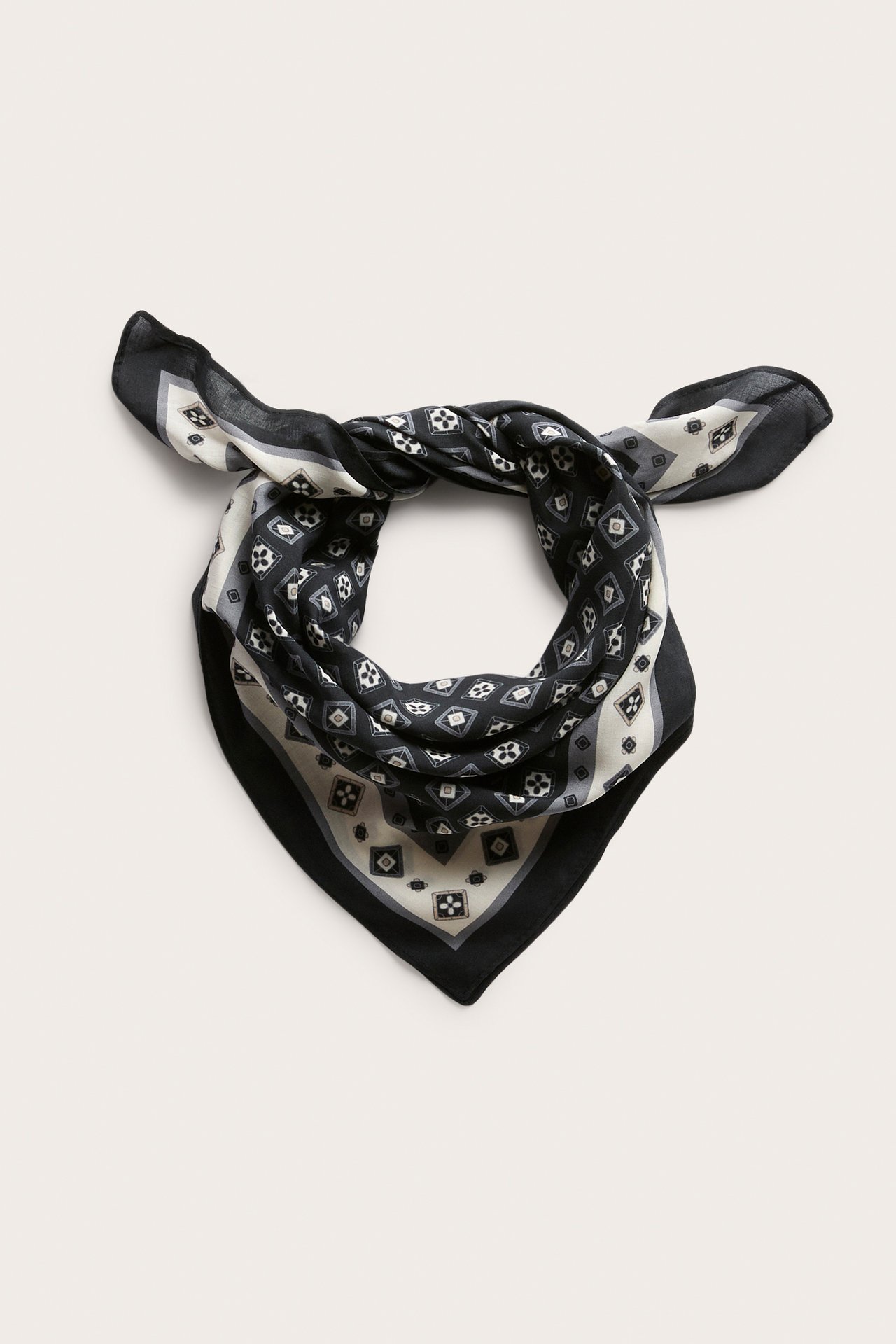 Edestä, musta, valkoinen ja harmaa geometrisesti kuvioitu bandana solmittuna.