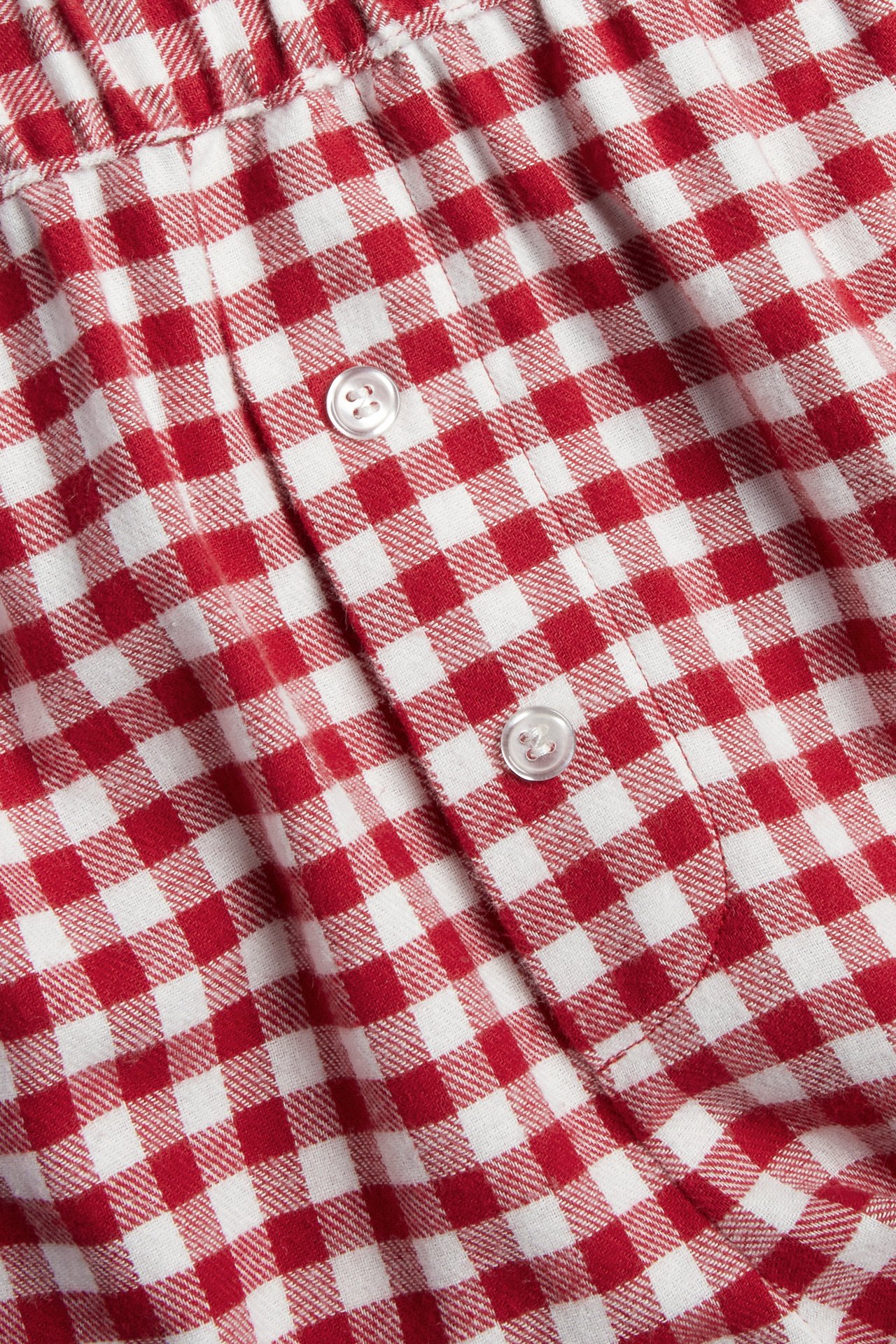 Lähikuva punavalkoisesta gingham-kankaasta kahdella pienellä valkoisella napilla.