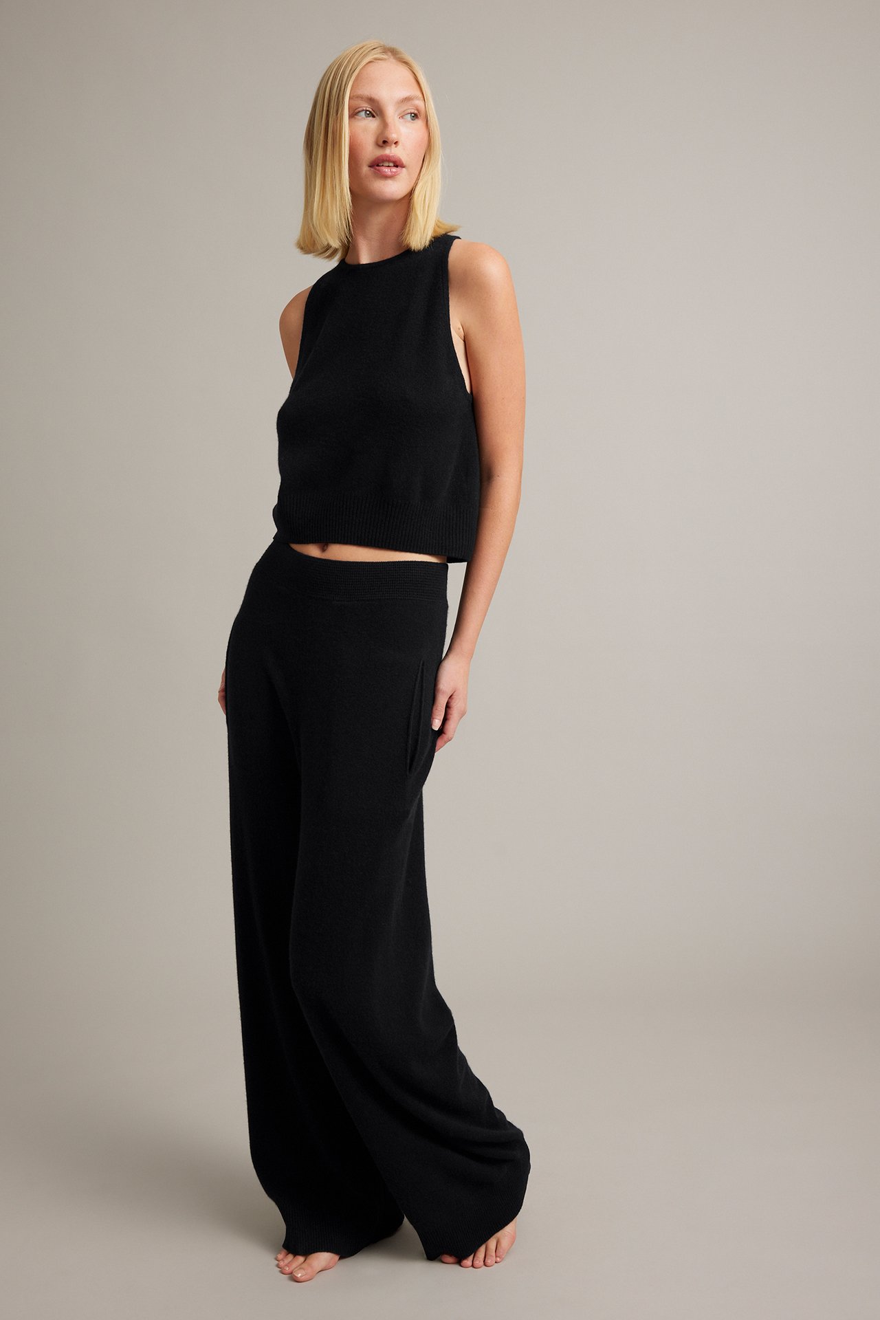 Frontbilde av en kvinne i svart strikket ermeløs crop top og matchende vide bukser.