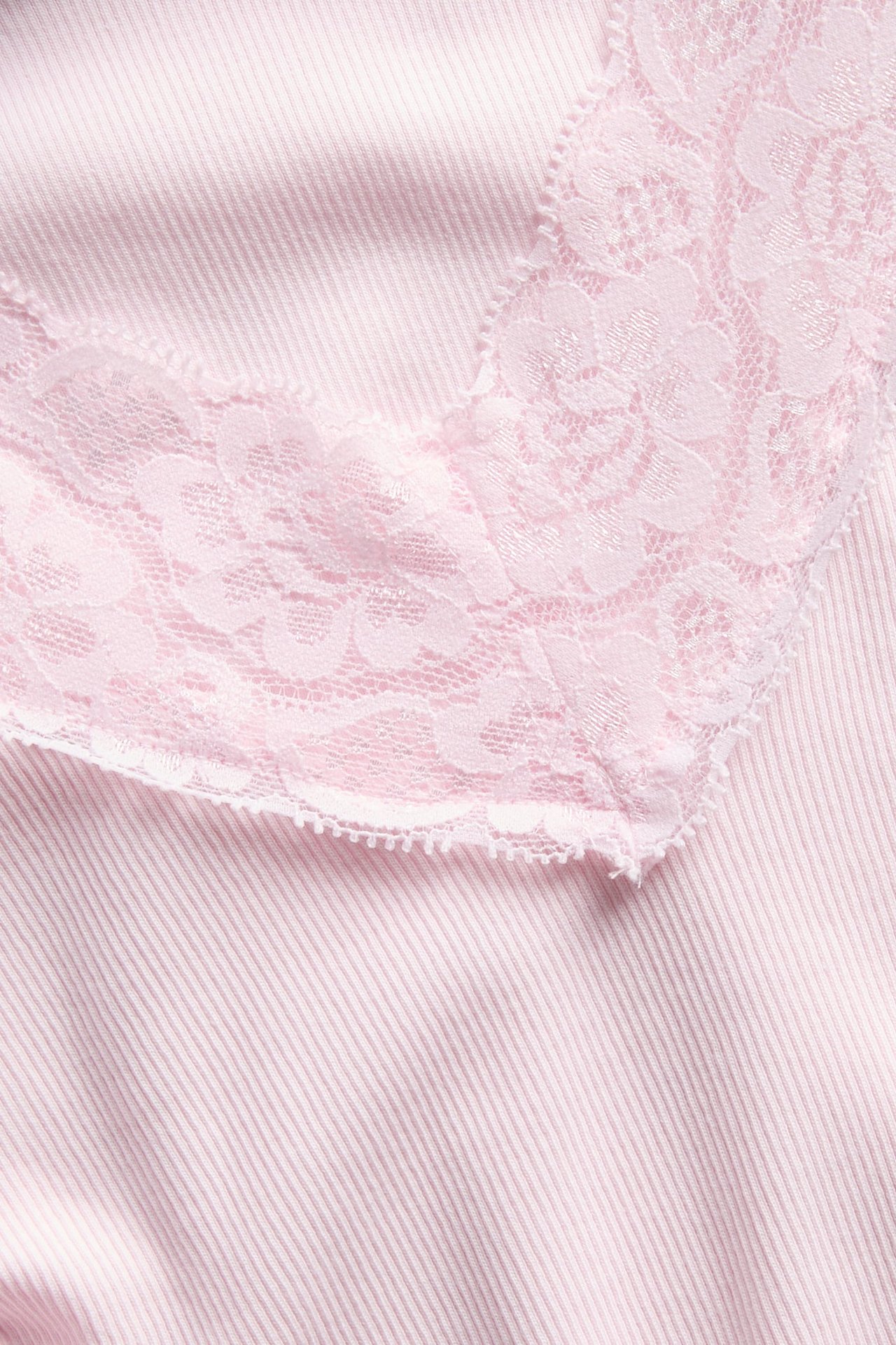 Nærbilde av et rosa ribbestrikket plagg med en blomstret blondekant.