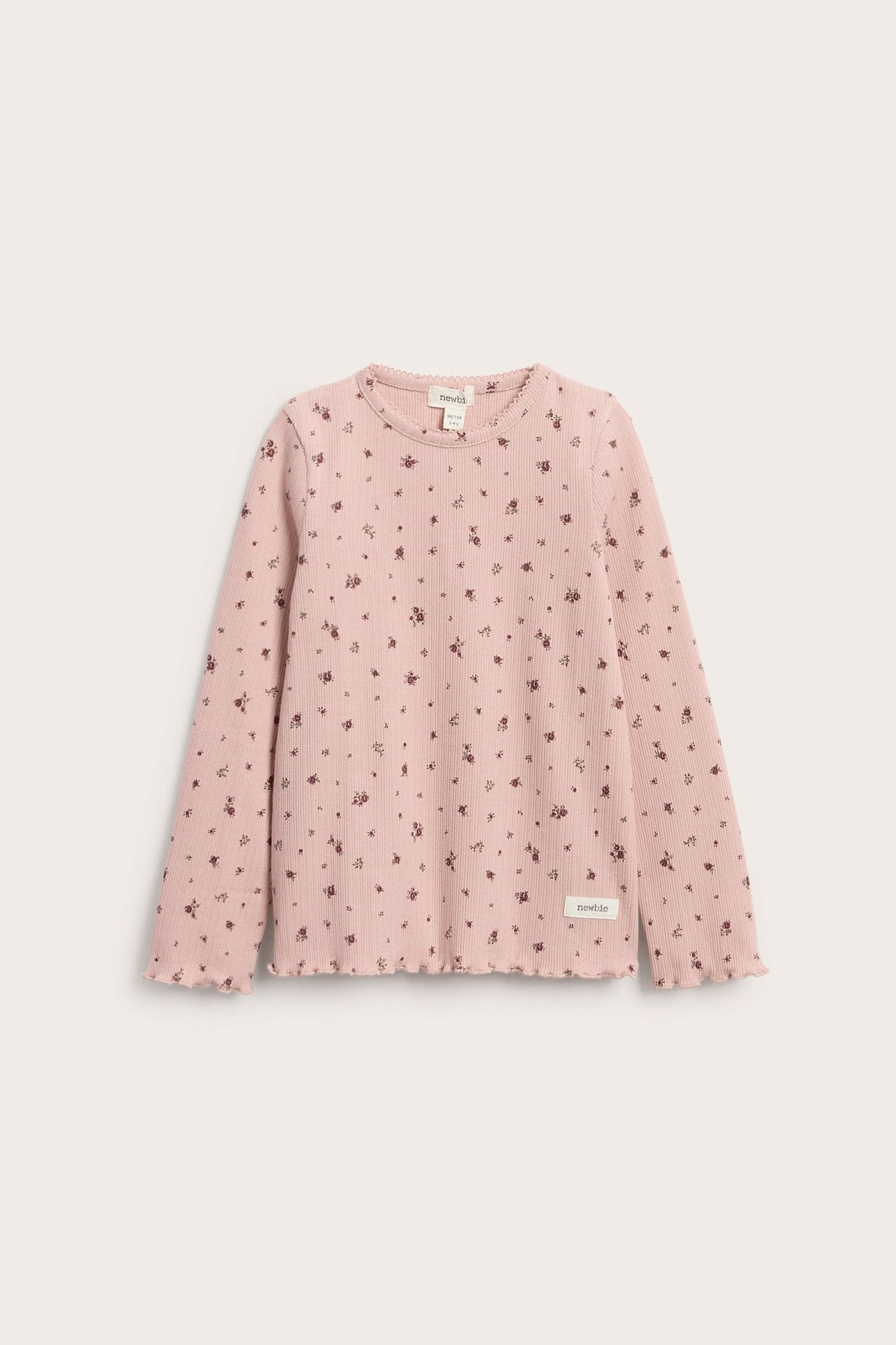 Framifrån, barns rosa ribbade långärmade topp med blommigt mönster och volang.