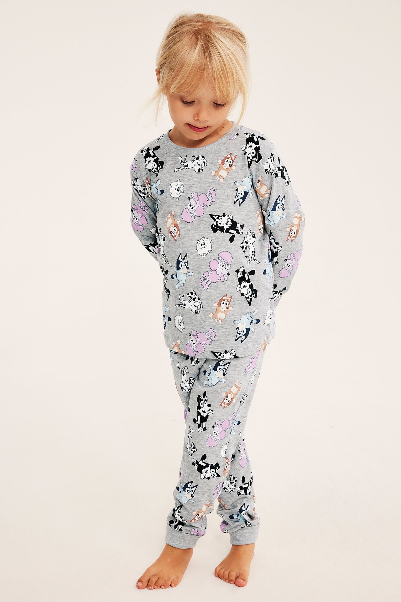 Framifrån, ett barn i grått pyjamasset med heltäckande tecknat hundmönster.