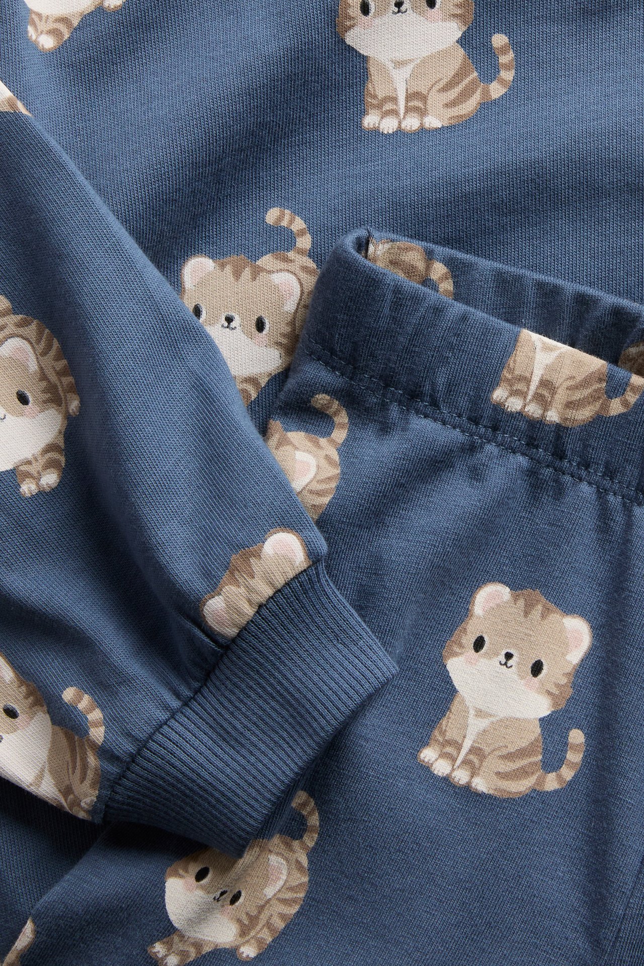Närbild på blå pyjamas i trikå med lång ärm, söta kattmönster och ribbade muddar.