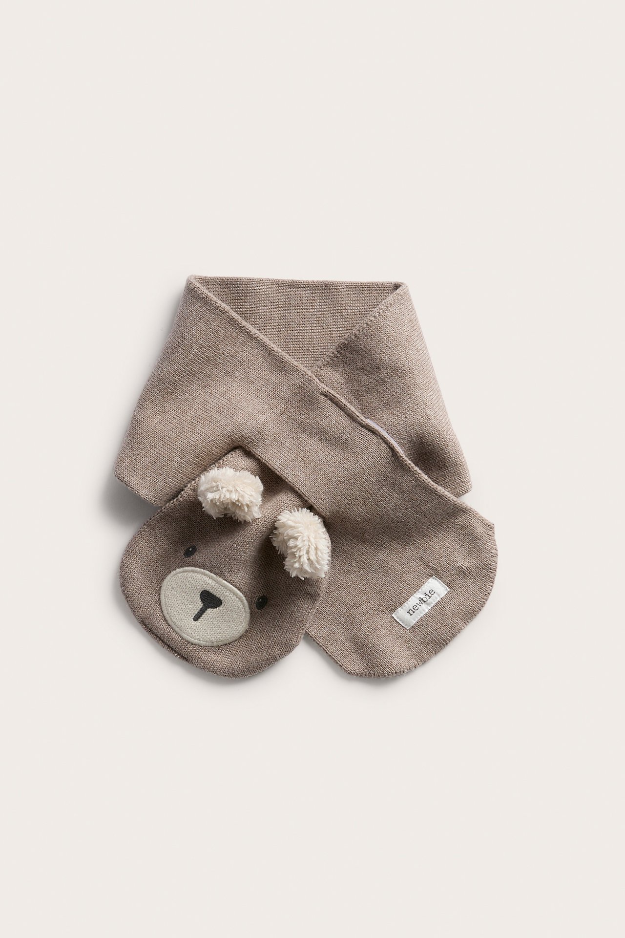 Neulottu vauvan beige kaulahuivi, jossa kirjailtu nallekasvot ja kaksi tupsukorvaa, edestä.
