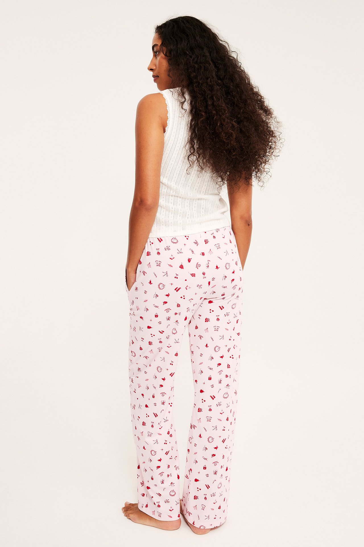 Ryggvy av kvinna i ljusrosa pyjamasbyxor med rött mönster och vitt ribbat linne.