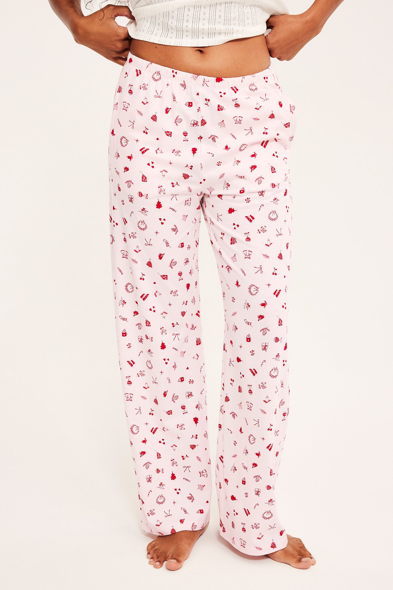 Frontvisning av lyserosa pyjamasbukser med rødt julemønster og en hvit teksturert crop top.
