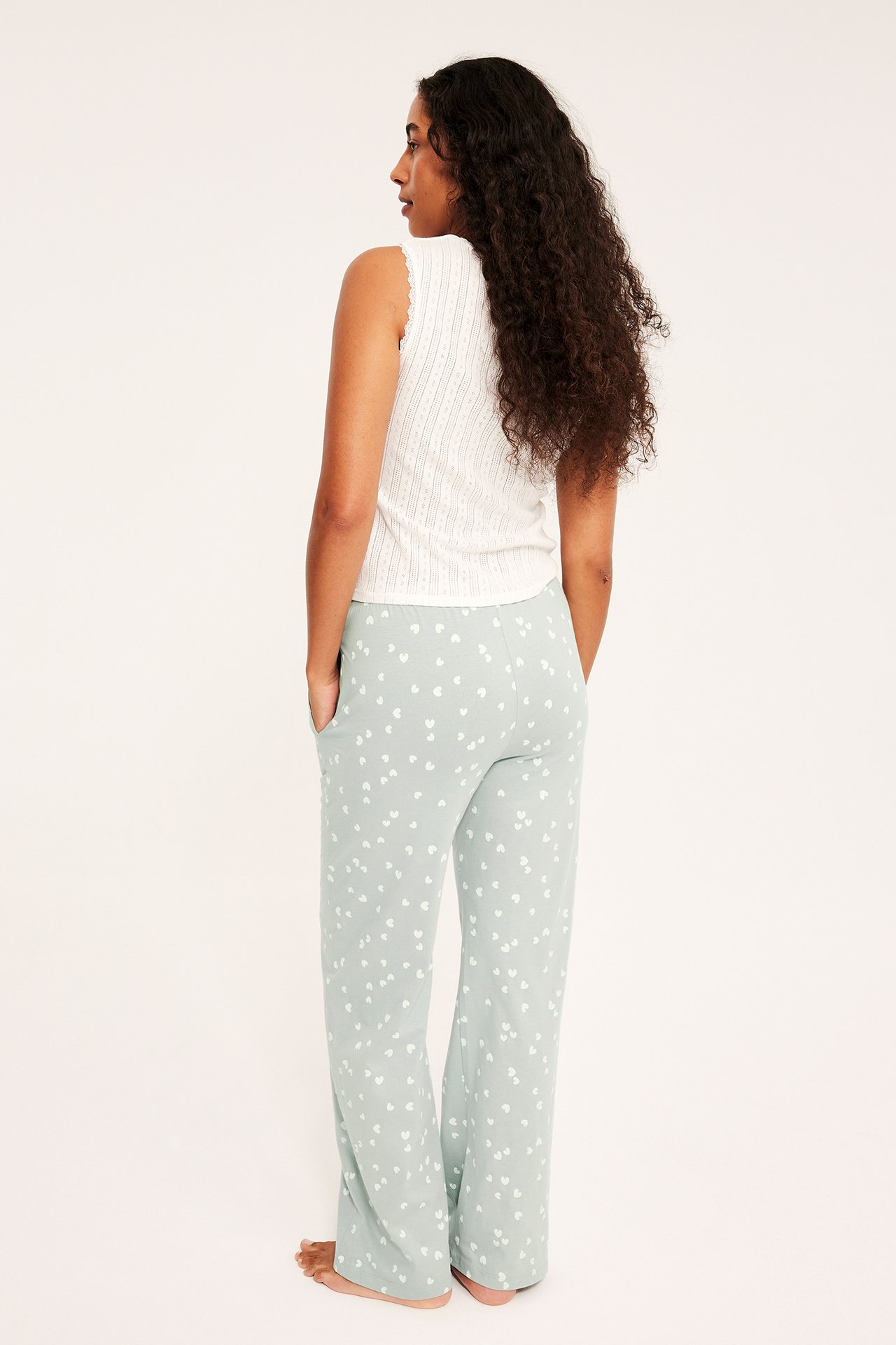 Ryggvy av en kvinna i ljusgröna pyjamasbyxor med hjärtmönster och ett vitt ribbat linne.