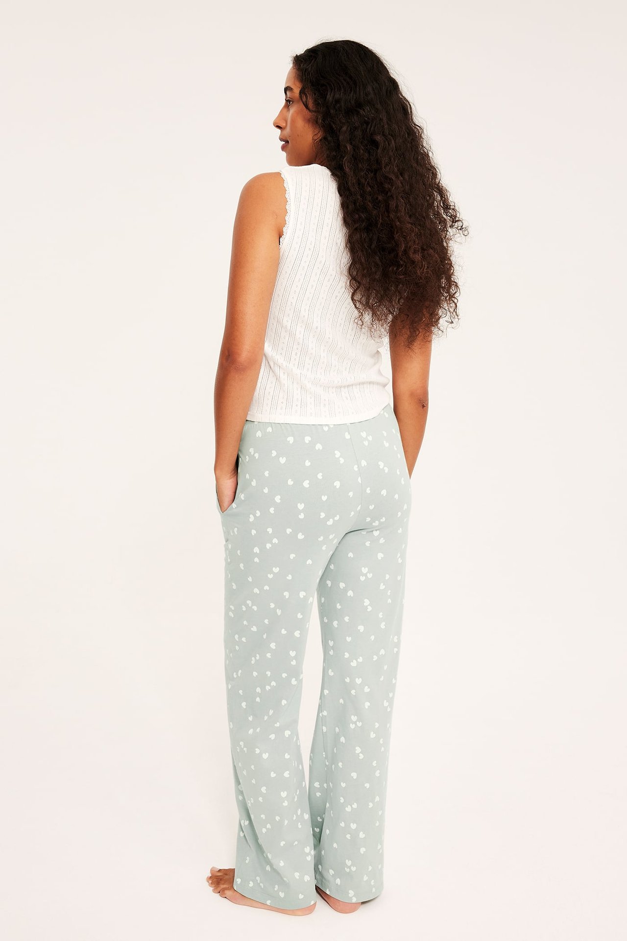 Ryggvy av en kvinna i ljusgröna pyjamasbyxor med hjärtmönster och ett vitt ribbat linne.