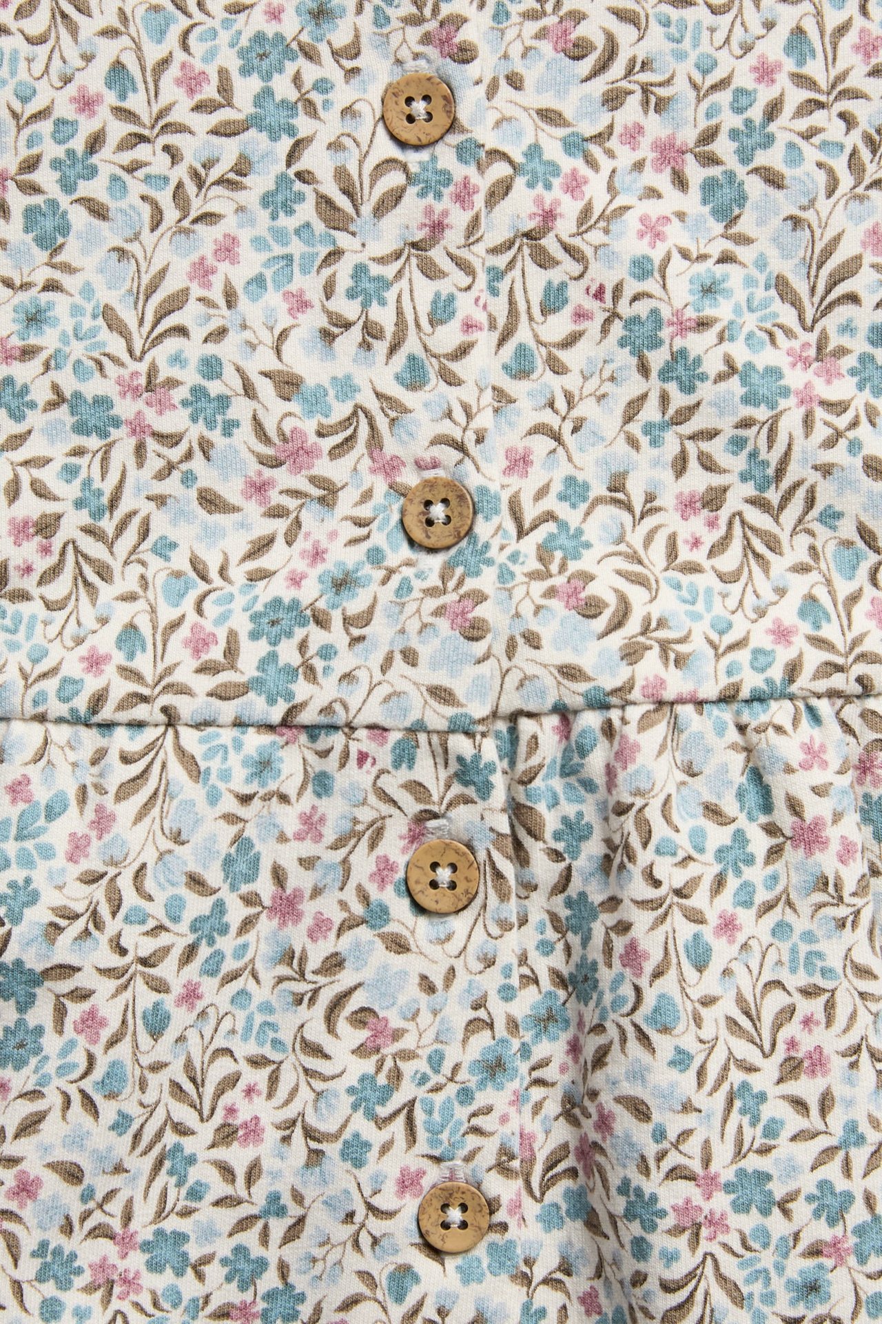 Nærbilde av kremfarget blomstret stoff med blå, rosa blomster, brune blader og treknapper.
