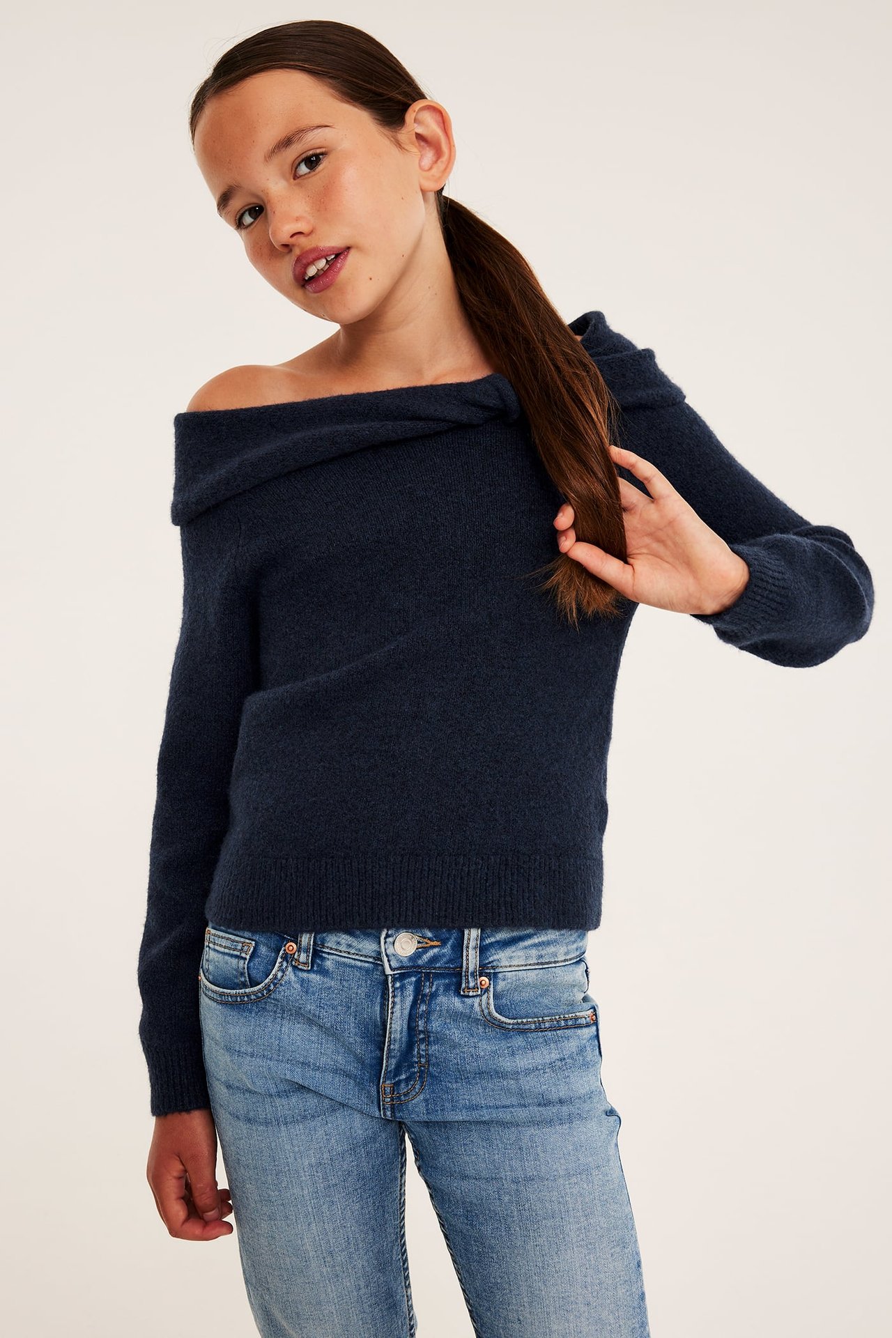 Framsida av en tjej som bär en mörkblå off shoulder-tröja och ljusblå jeans.