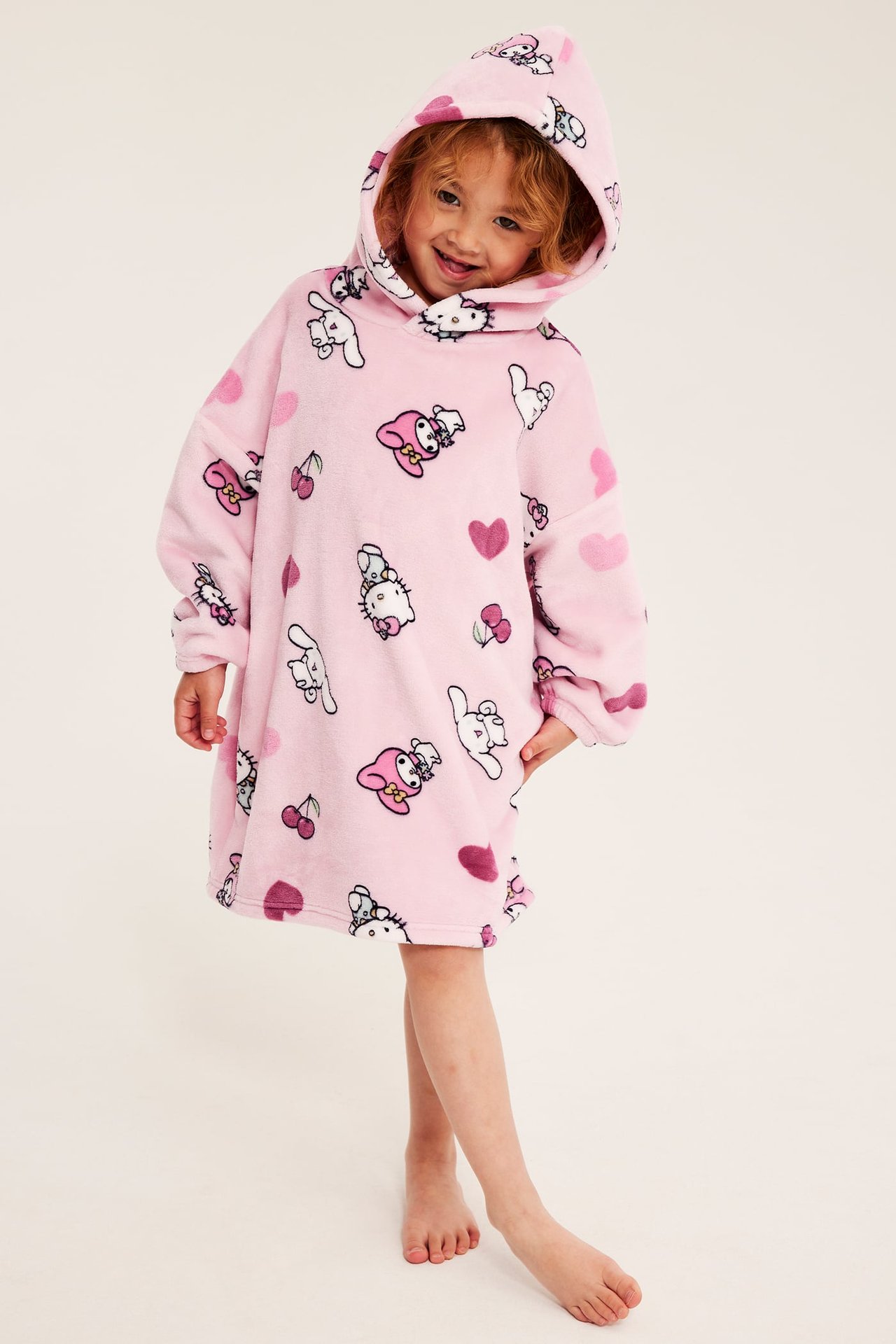 Frontbilde av et barn i en rosa lodden overdimensjonert hettegenser-kjole med Hello Kitty-mønster.