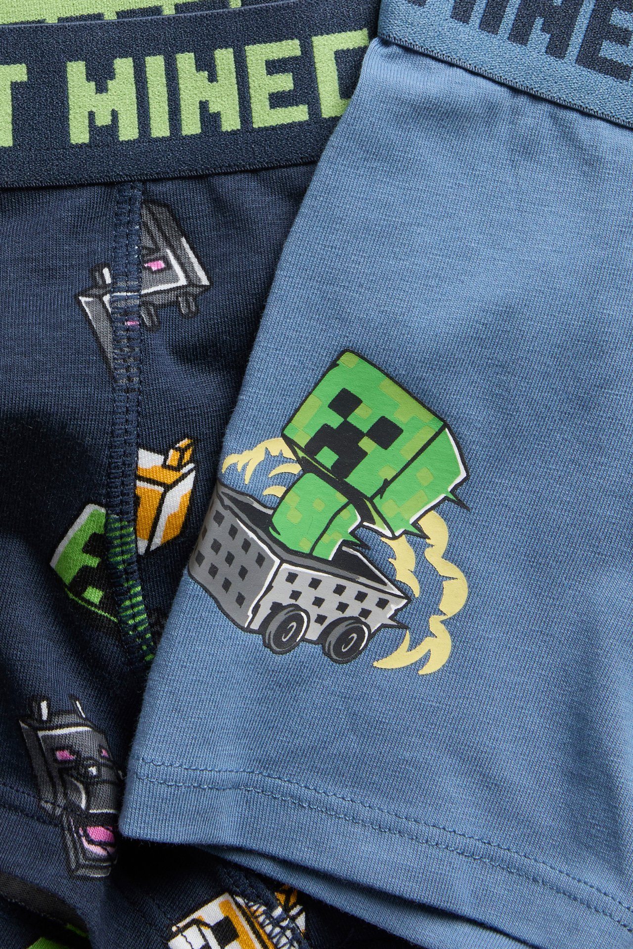 Lähikuva lasten sinisistä Minecraft-bokserishortseista Creeper-painatuksella, tummansinisen parin vieressä.