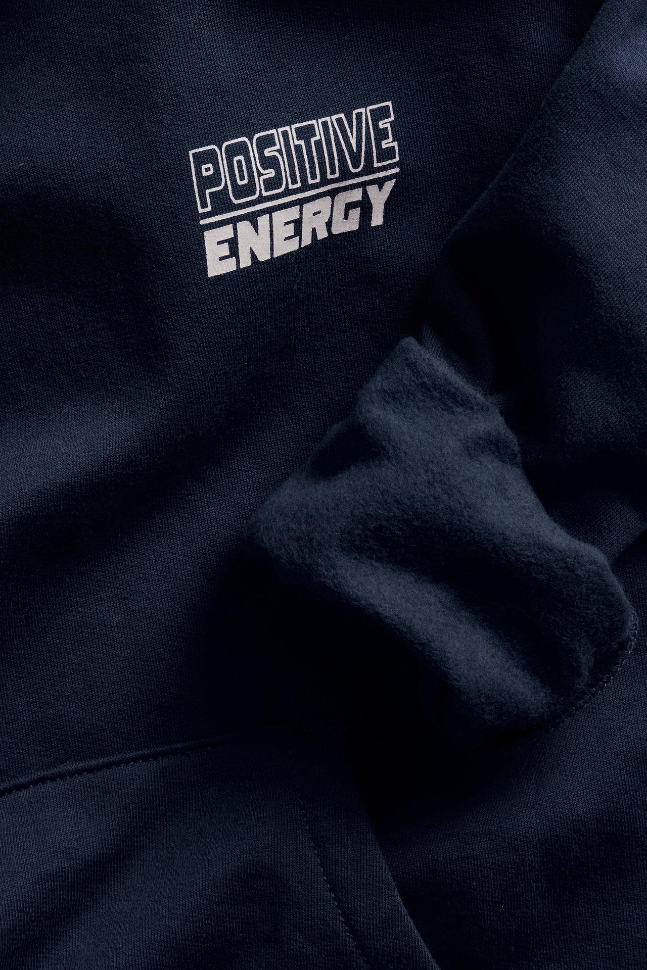 Zbliżenie na granatową bluzę z kapturem z białym napisem „POSITIVE ENERGY” z przodu.