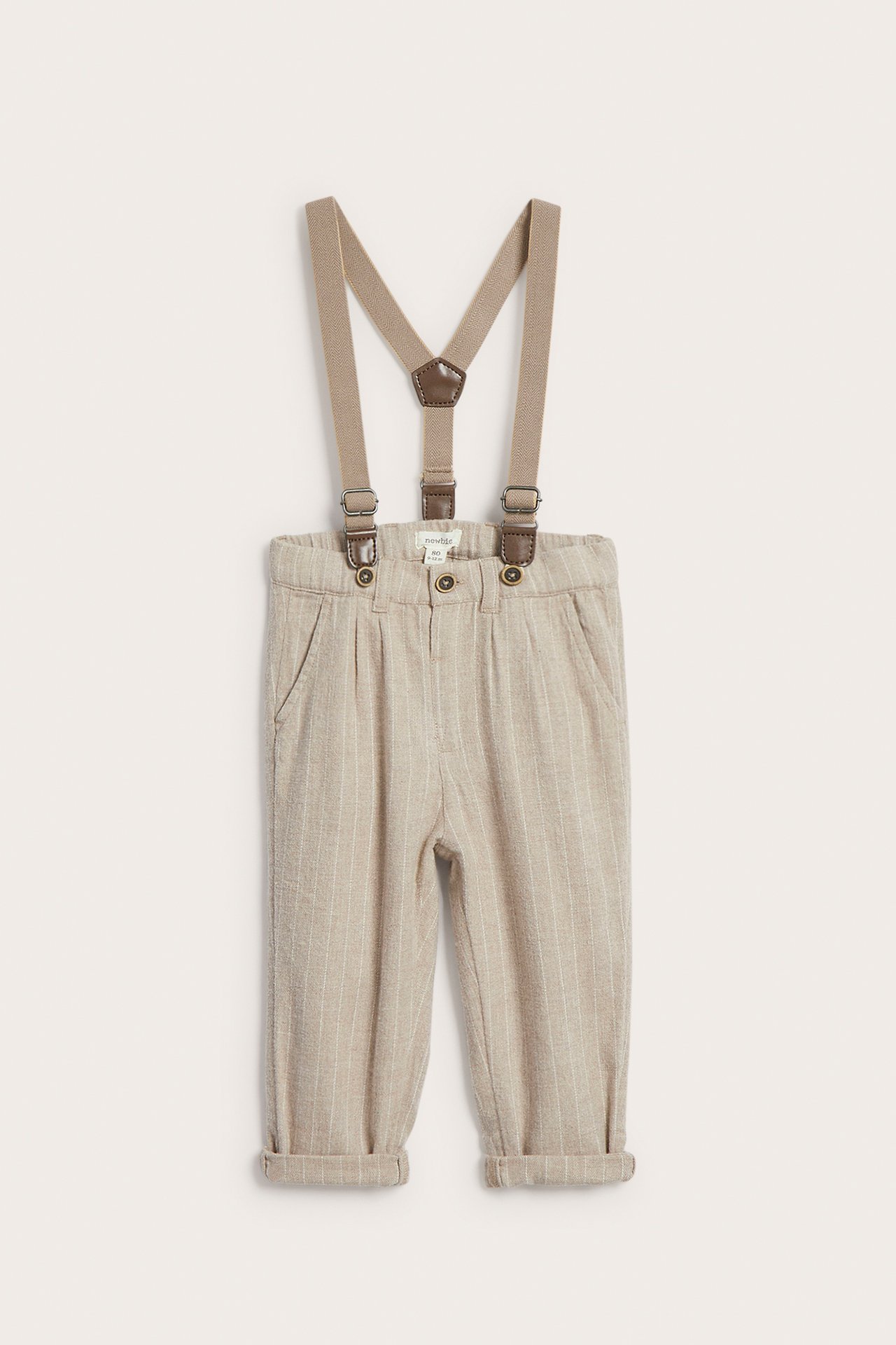 Frontvisning av baby pinstripede beige bukser med seler og oppbrettede ankler.