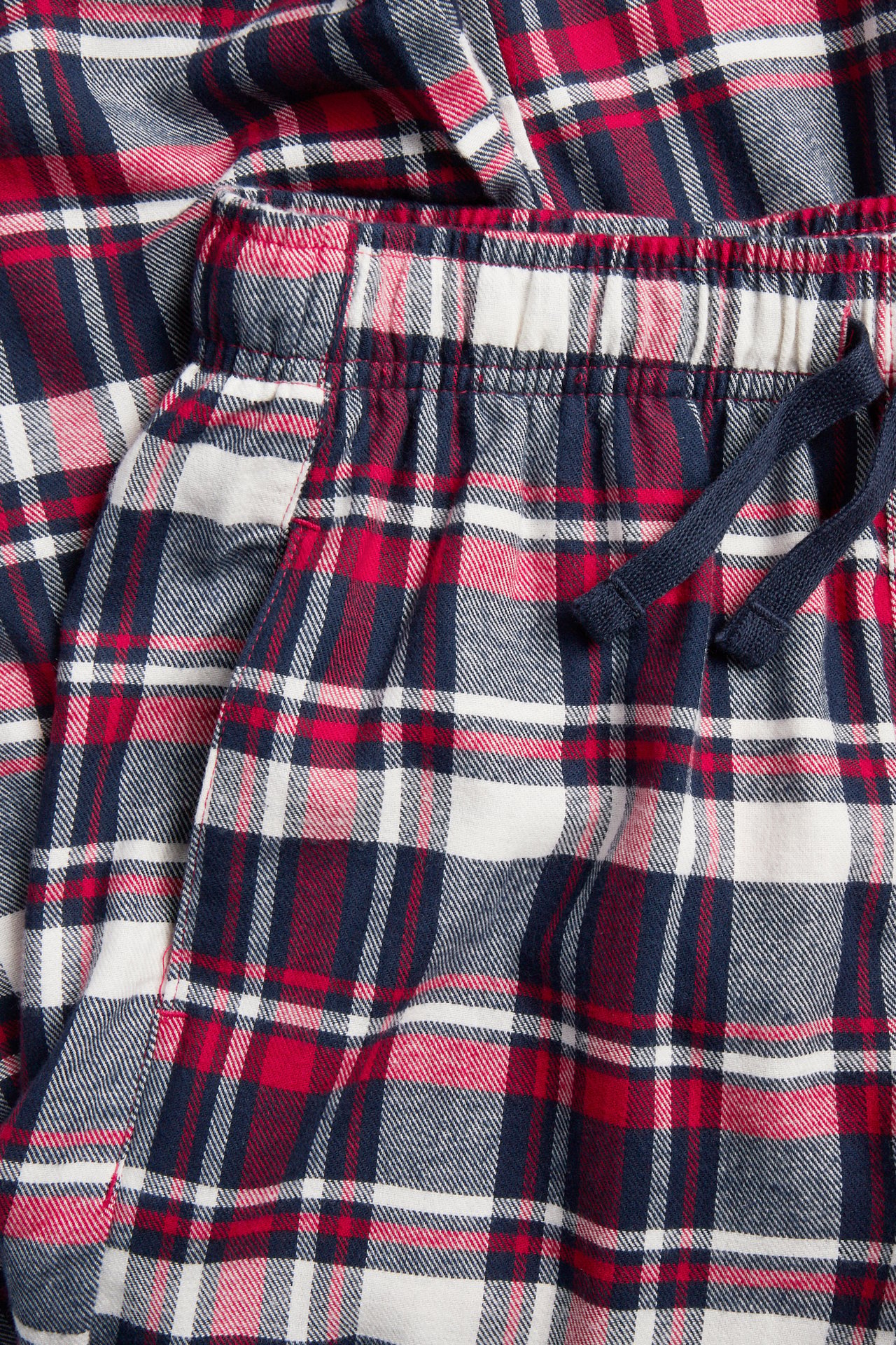 Närbild på röda, marinblå och vita rutiga pyjamasbyxor med resår i midjan och marinblå dragsko.