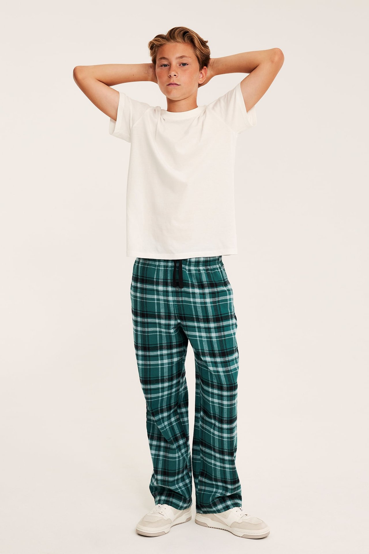 Frontbilde av grønne rutete pyjamasbukser på gutt, med hvit t-skjorte og hvite joggesko.