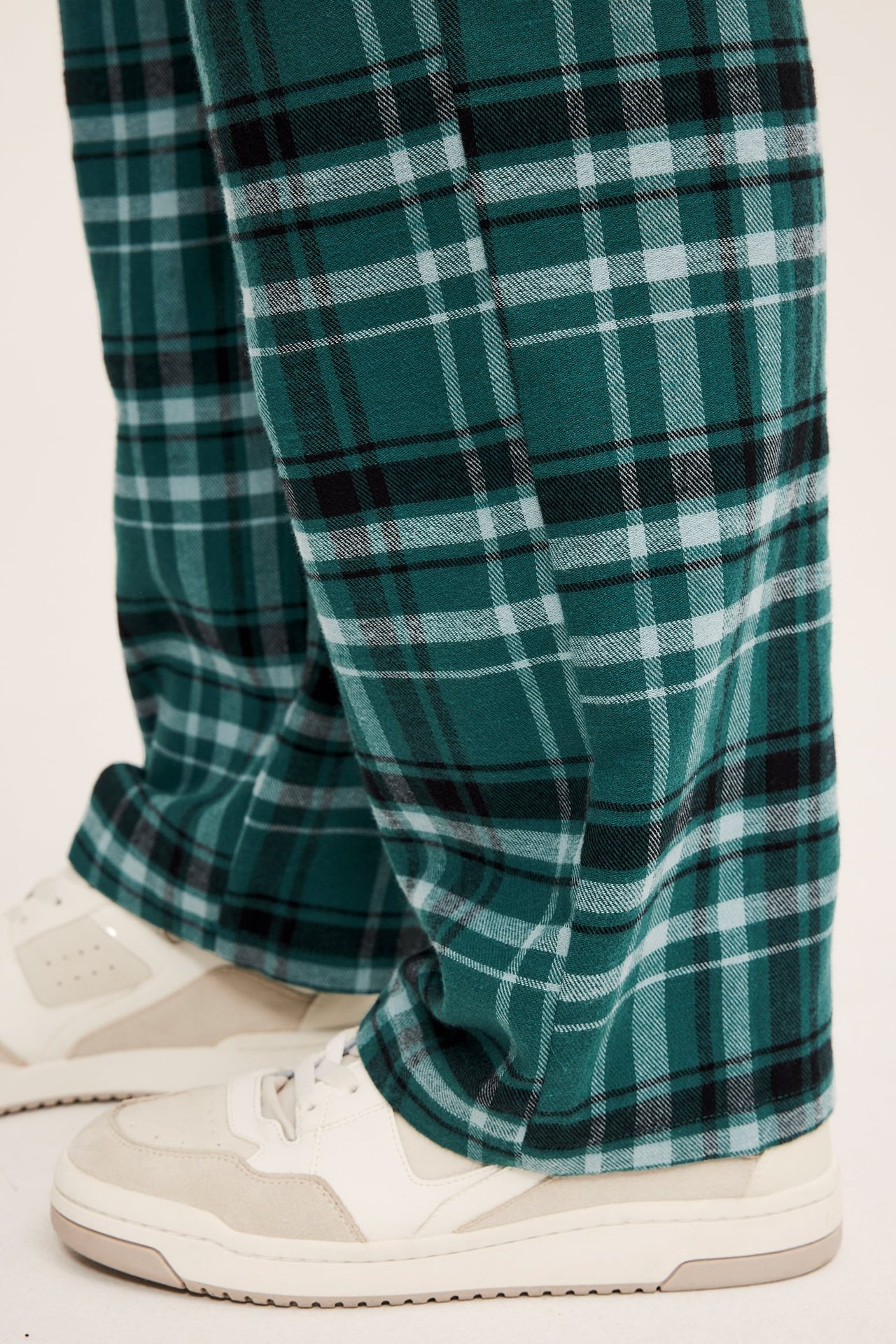 Nærbilde av grønne, svarte og hvite rutete bukser brukt med hvite sneakers.