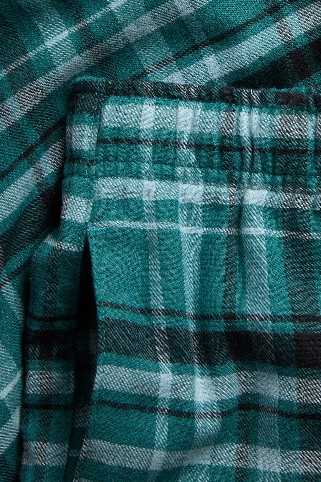Nærbilde av turkise, svarte og hvitrutete pyjamasbukser med elastisk linning.