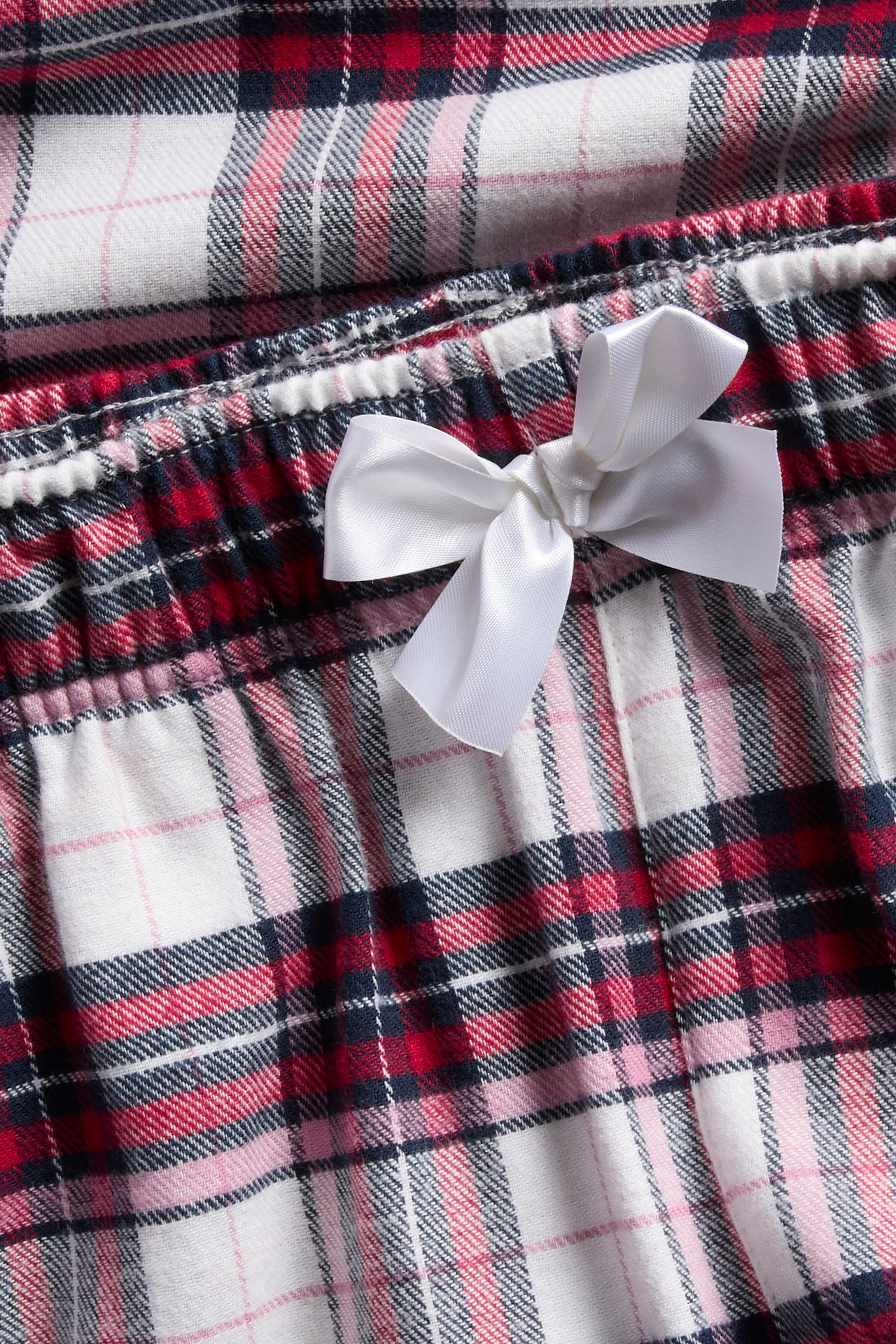 Lähikuva punaisista, valkoisista, laivastonsinisistä ja pinkeistä ruudullisista flanellipyjamahousuista, joissa valkoinen satiininauha.