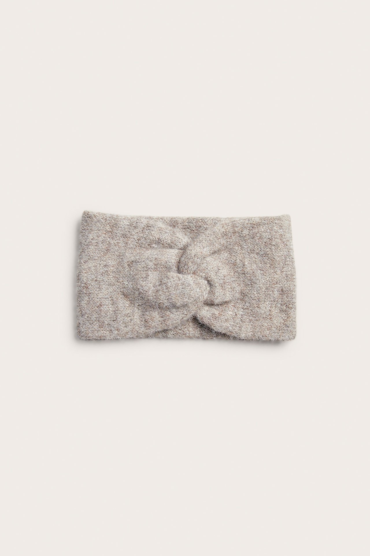 Framifrån: Melerat beigt stickat pannband med knutdetalj.