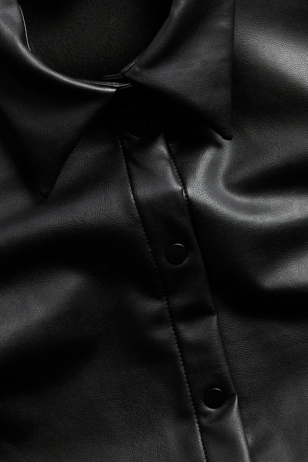 Zbliżenie czarnej koszuli ze sztucznej skóry z kołnierzem i czarnymi guzikami.