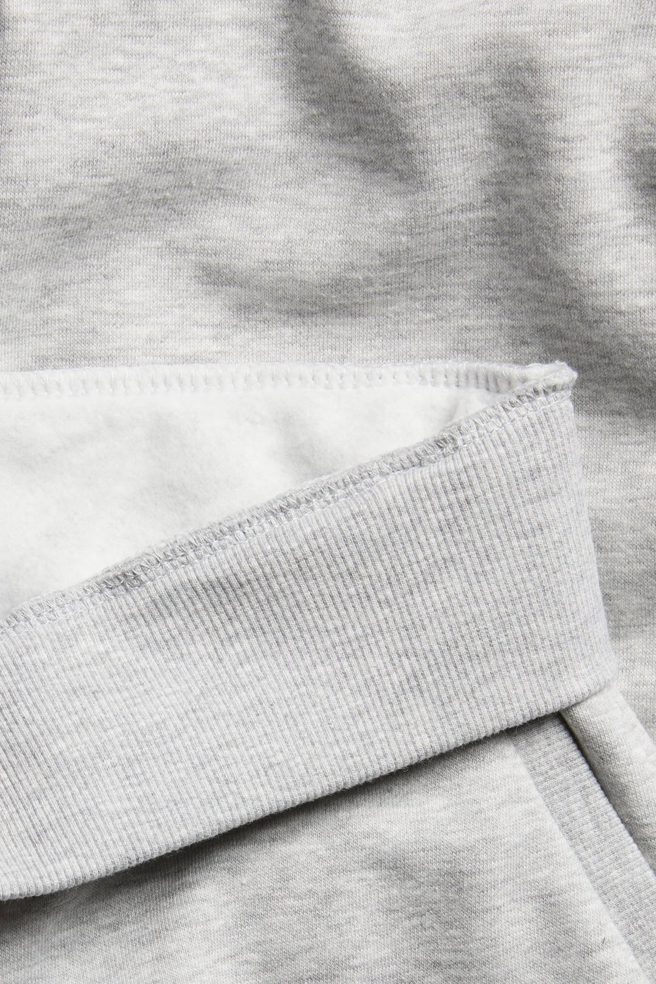 Lähikuva harmaasta meleeratusta collegepaidasta, jossa näkyy jerseymateriaali, ribbineulos ja harjattu vuori.