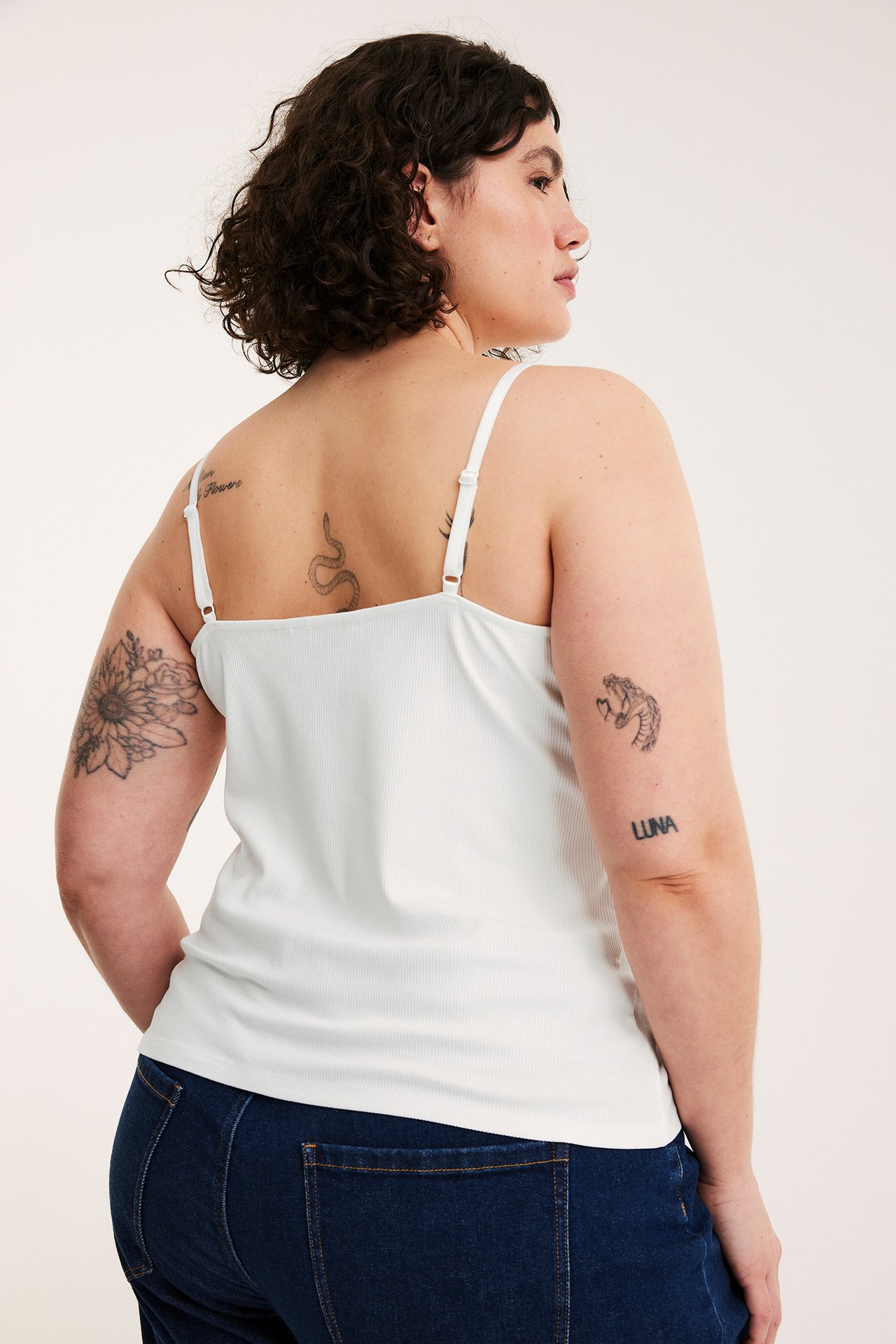 Bakfra kvinne i off-white ribbet linne med justerbare stropper og mørkeblå jeans.