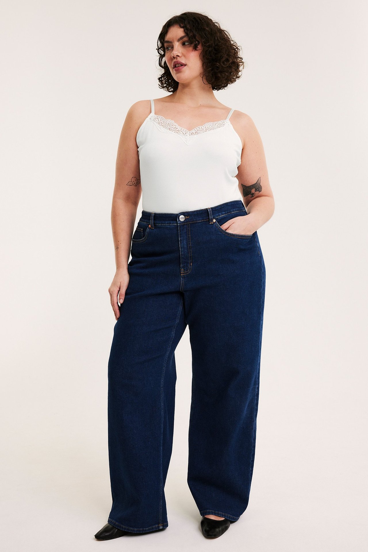 Framifrån: kvinna i offwhite ribbat spetslinne, mörkblå vida jeans och svarta platta skor.